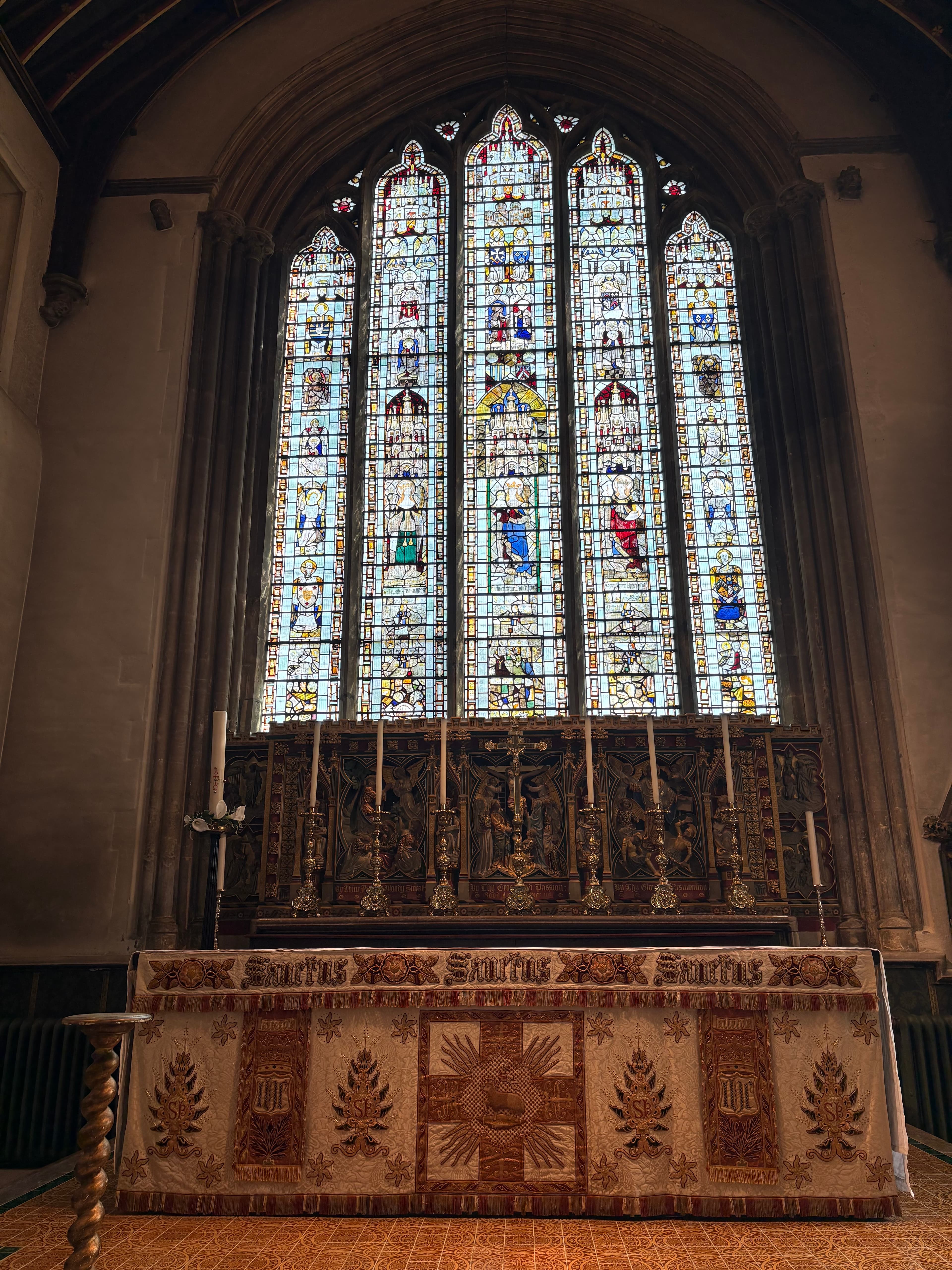 A tall five-light stained-glass window above an embroidered hanging
