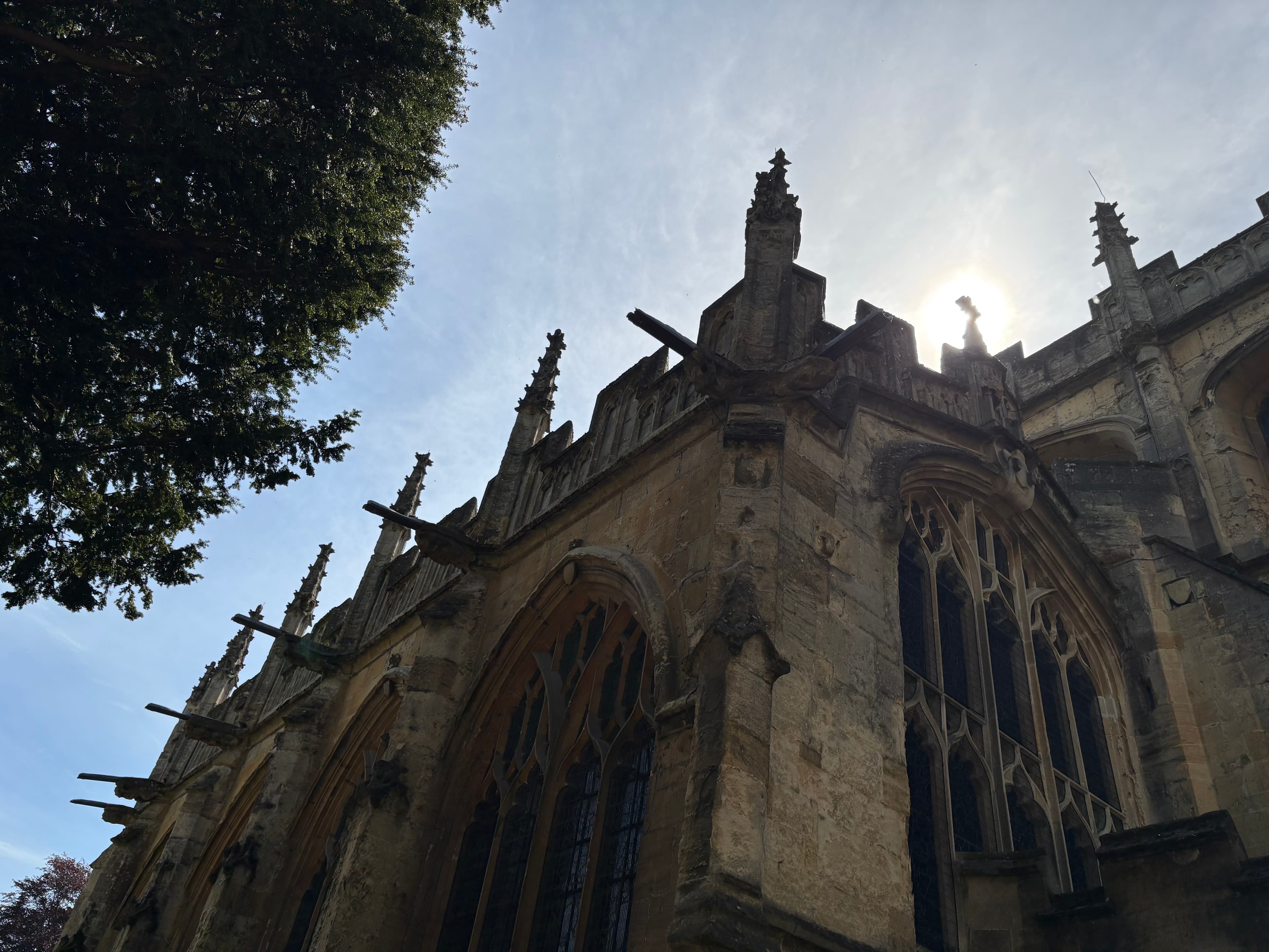 Late-afternoon backlit view of the south side of St John the Baptist Cirencester — pinnacles and traceried windows in silhouette