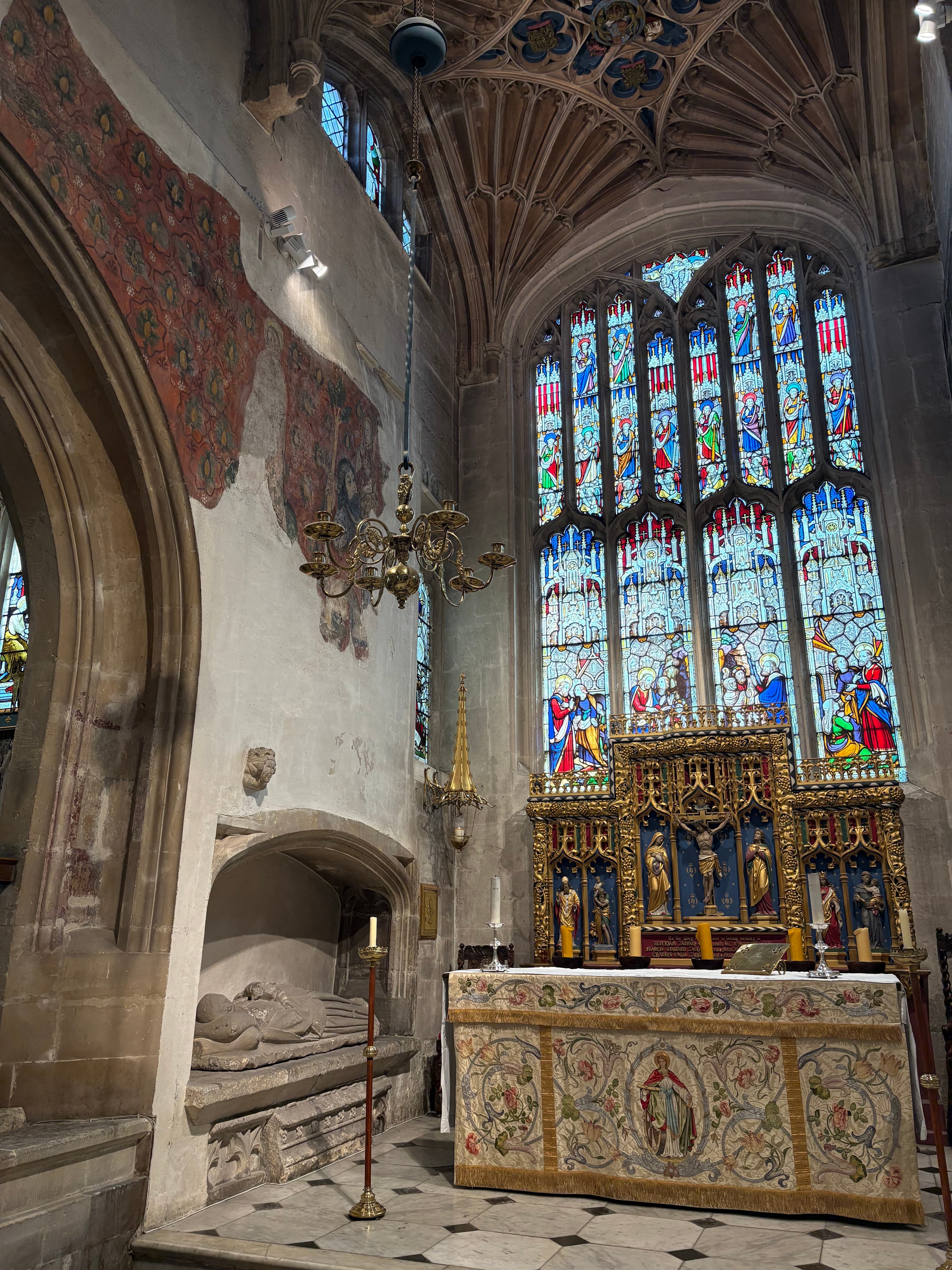 A large Victorian stained-glass window above a richly embroidered tapestry hanging