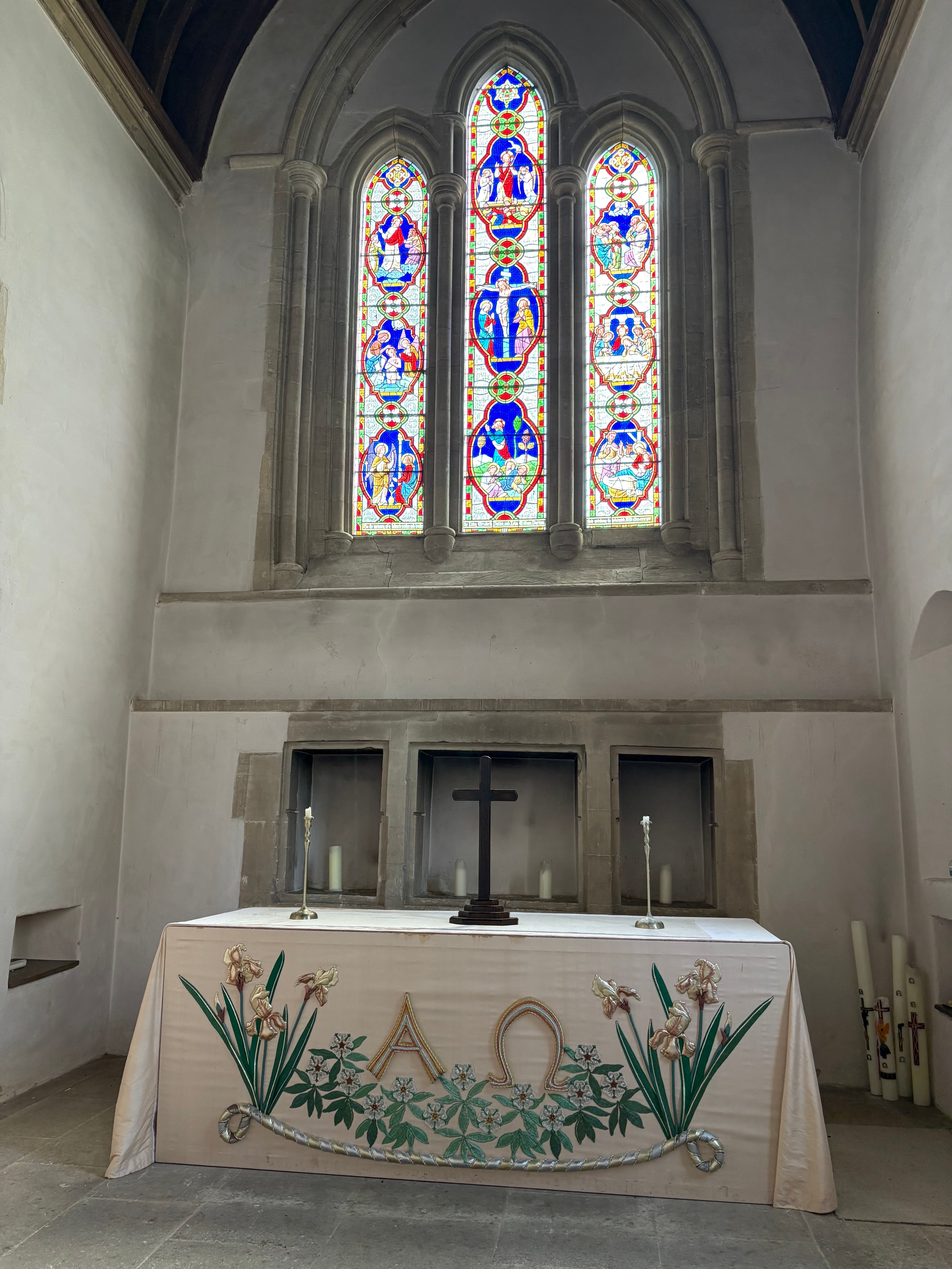 The east window above the altar — three-light stained glass with an embroidered altar frontal beneath