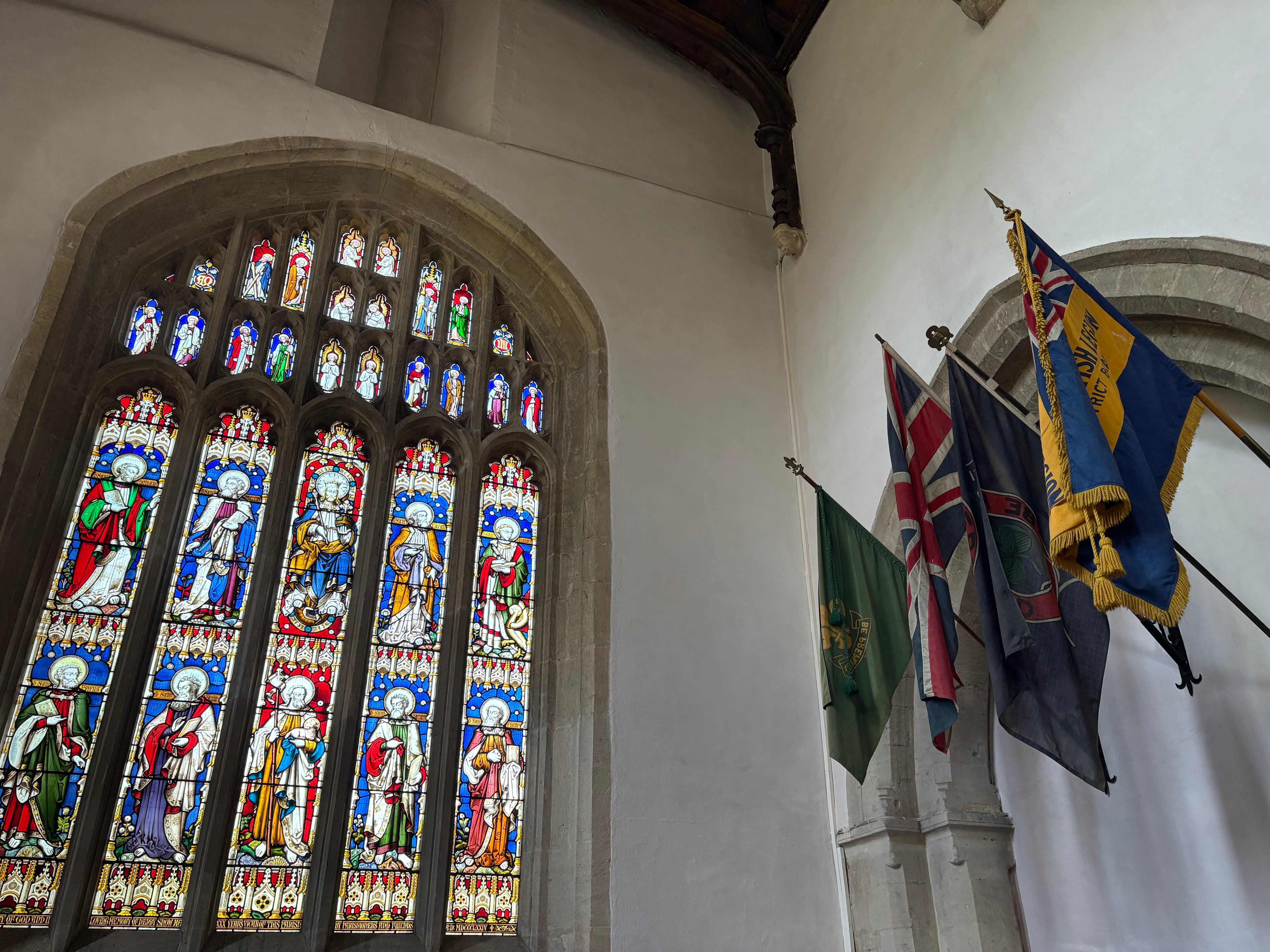 A large stained-glass window in the south aisle of St Mary's, with regimental flags hung alongside
