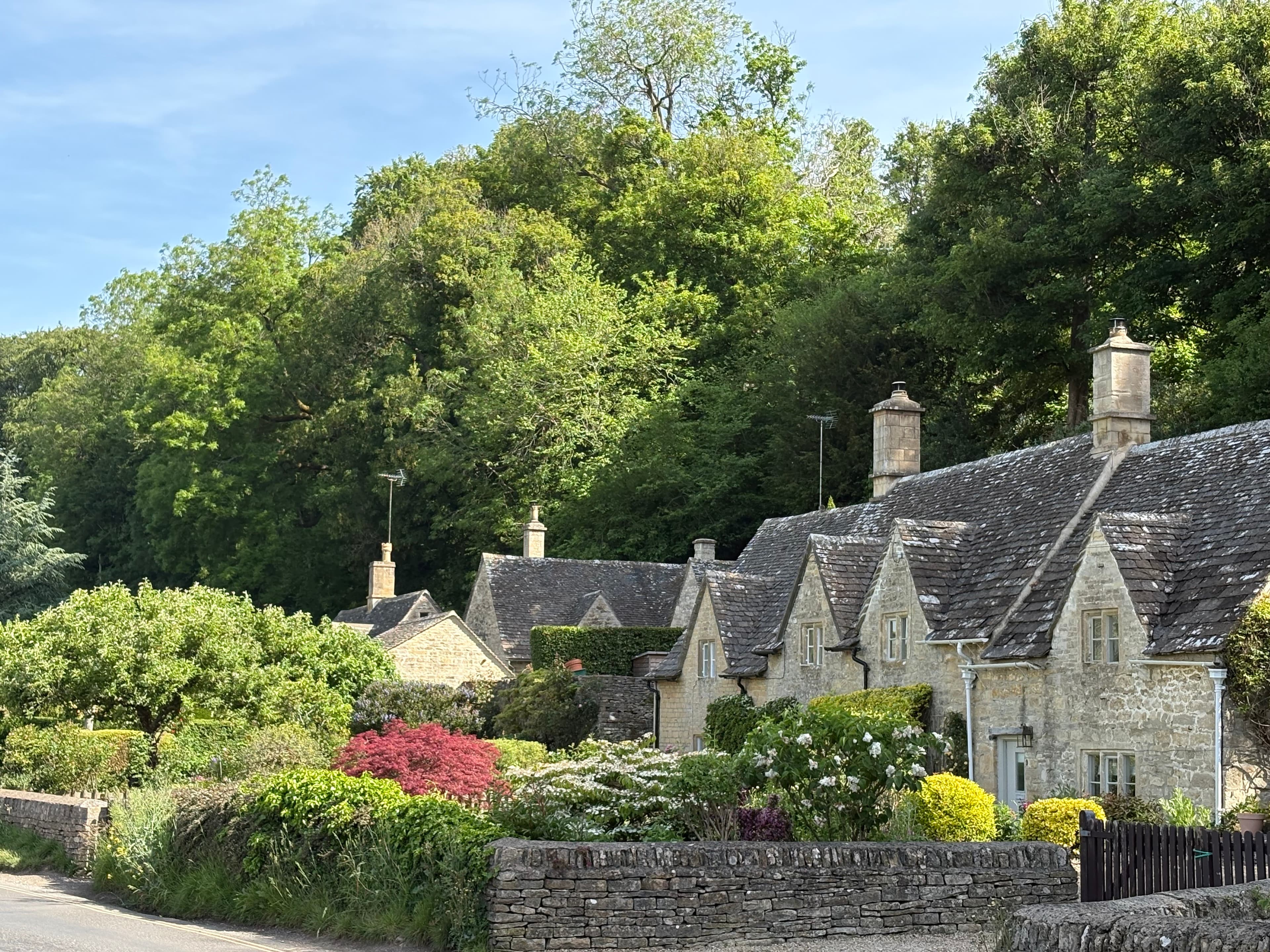 A row of gabled Cotswold cottages in Bibury with well-tended front gardens in early summer