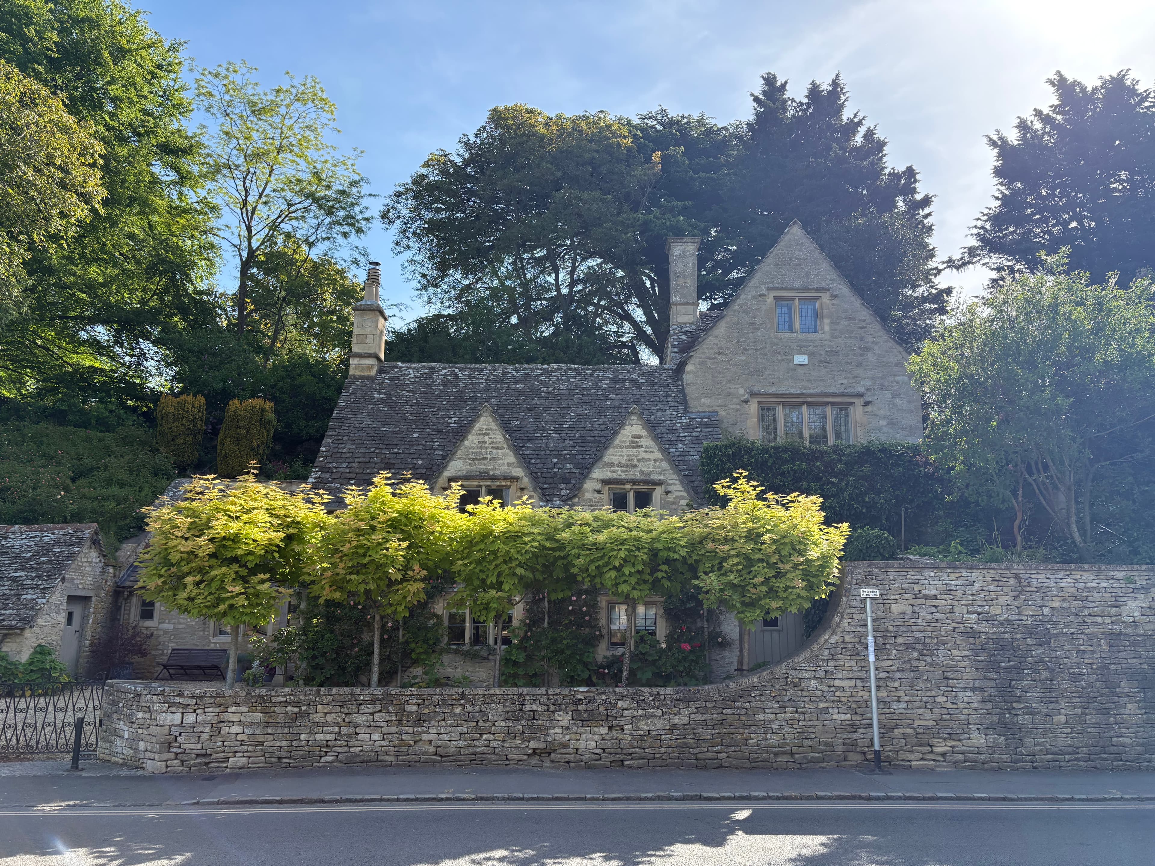A Cotswold-stone cottage in Bibury behind a row of espaliered trees