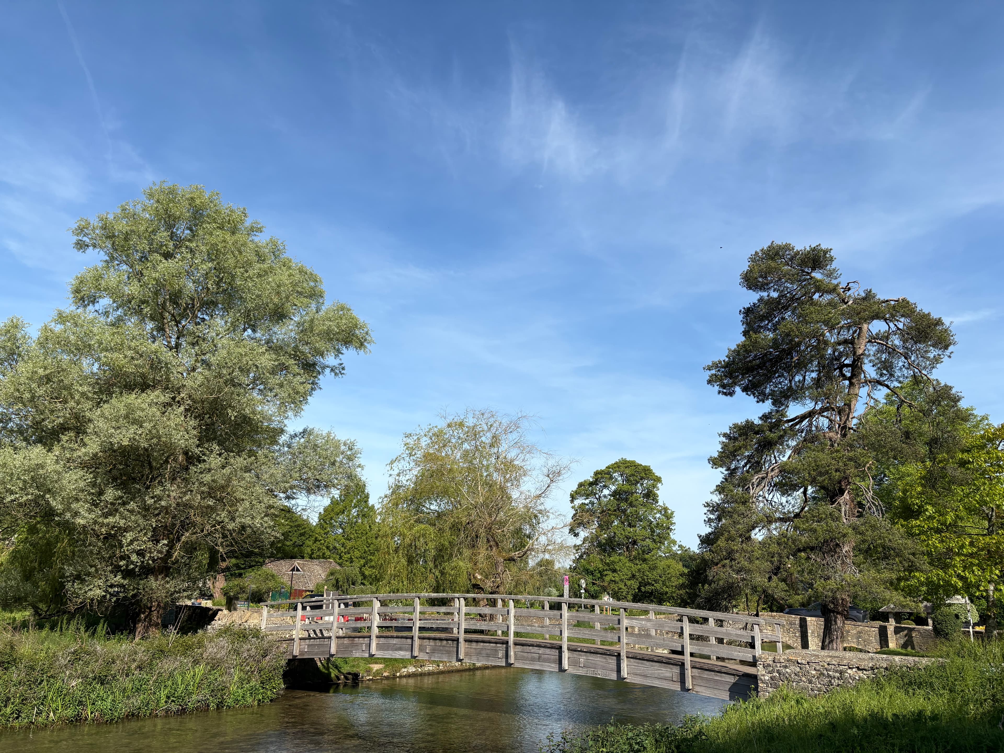 The wooden footbridge across the Coln, with willows on the bank