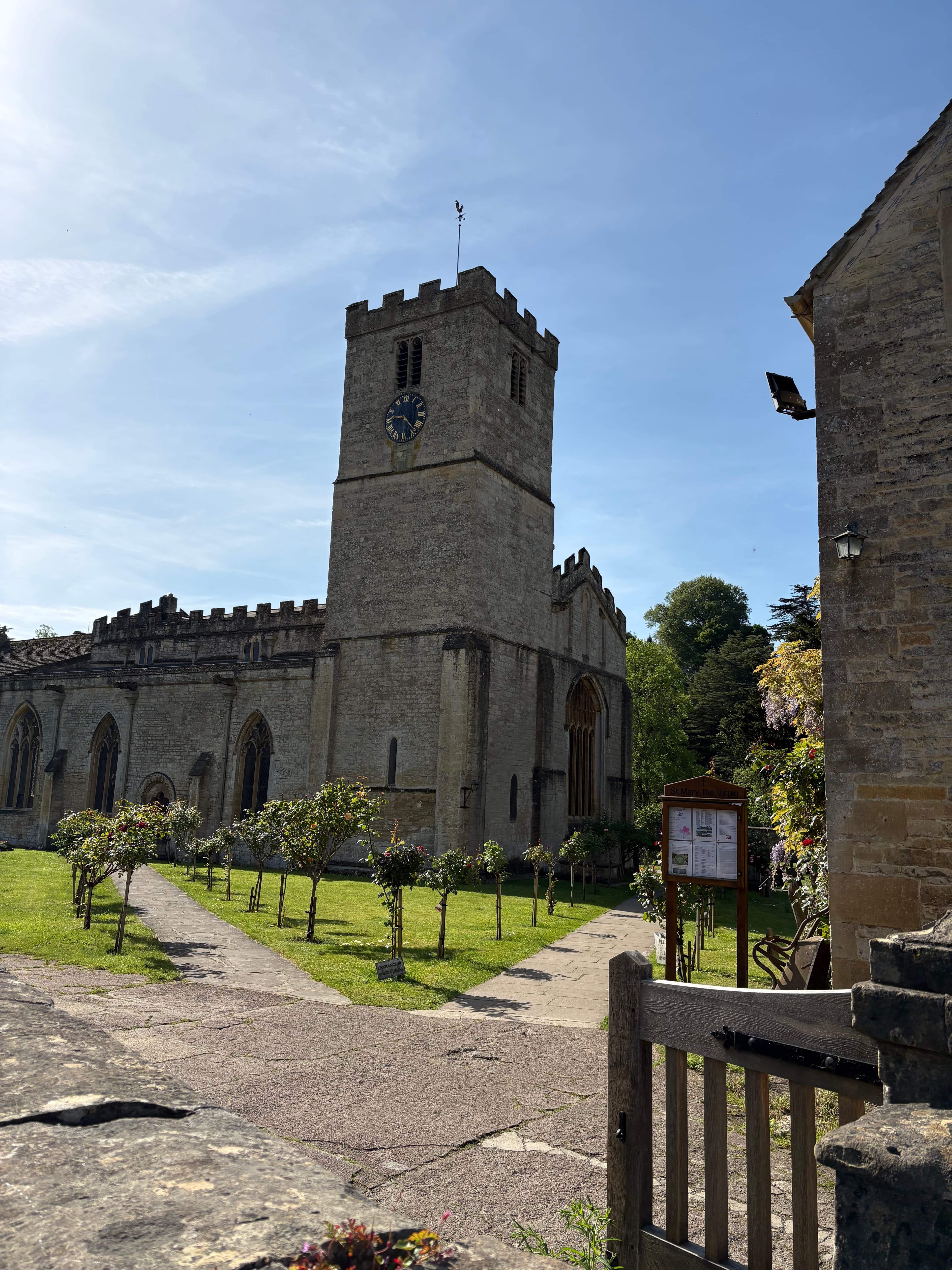 St Mary's Church, Bibury — tower with clock face, seen across the churchyard
