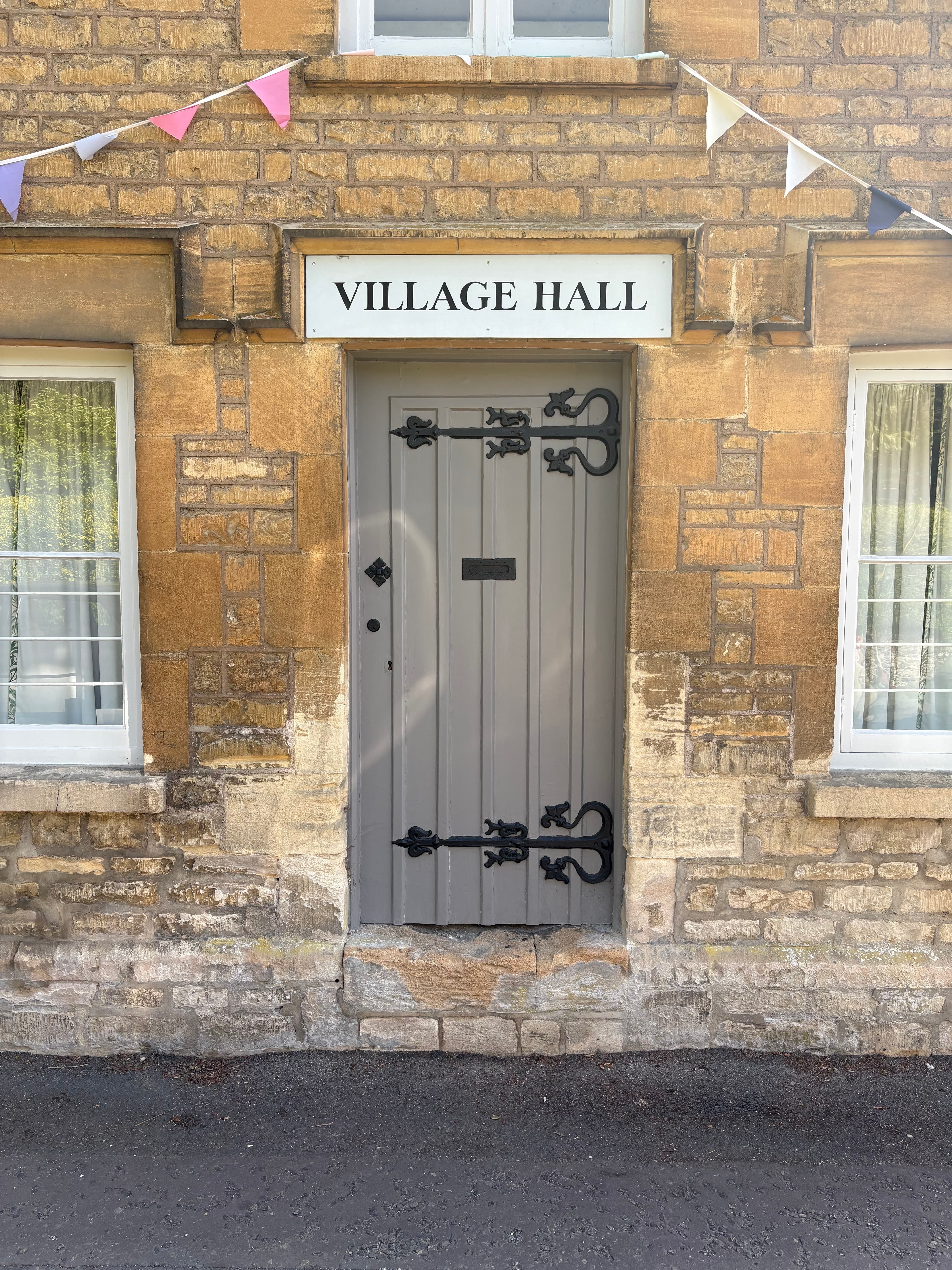 The painted Village Hall sign and door on Bibury's main street, hung with bunting
