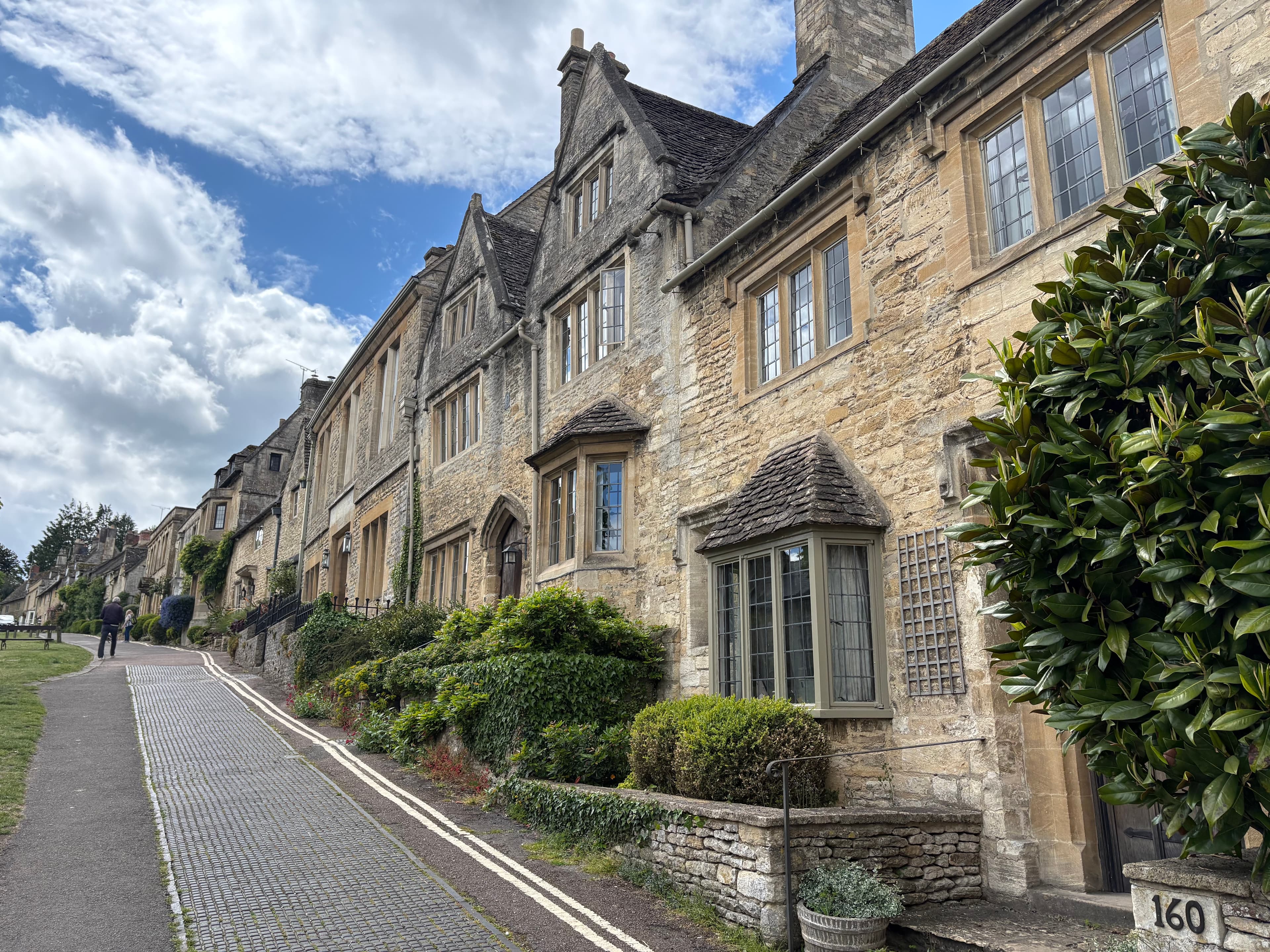 A row of honey-stone cottages set behind a verge on the upper high street