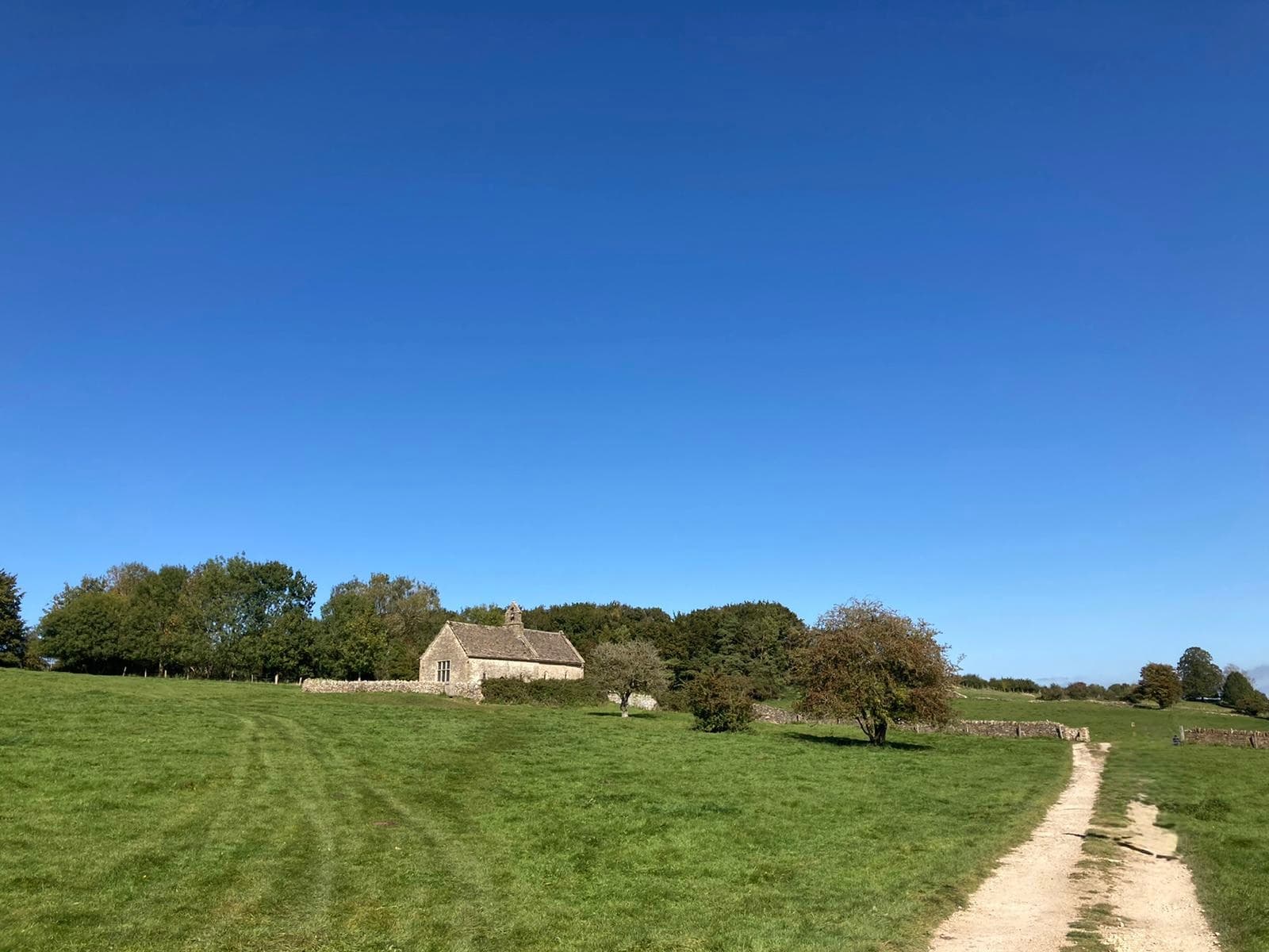 St Oswald's Church at Widford — a small medieval church standing alone in fields a mile east of Burford, framed by trees and a footpath