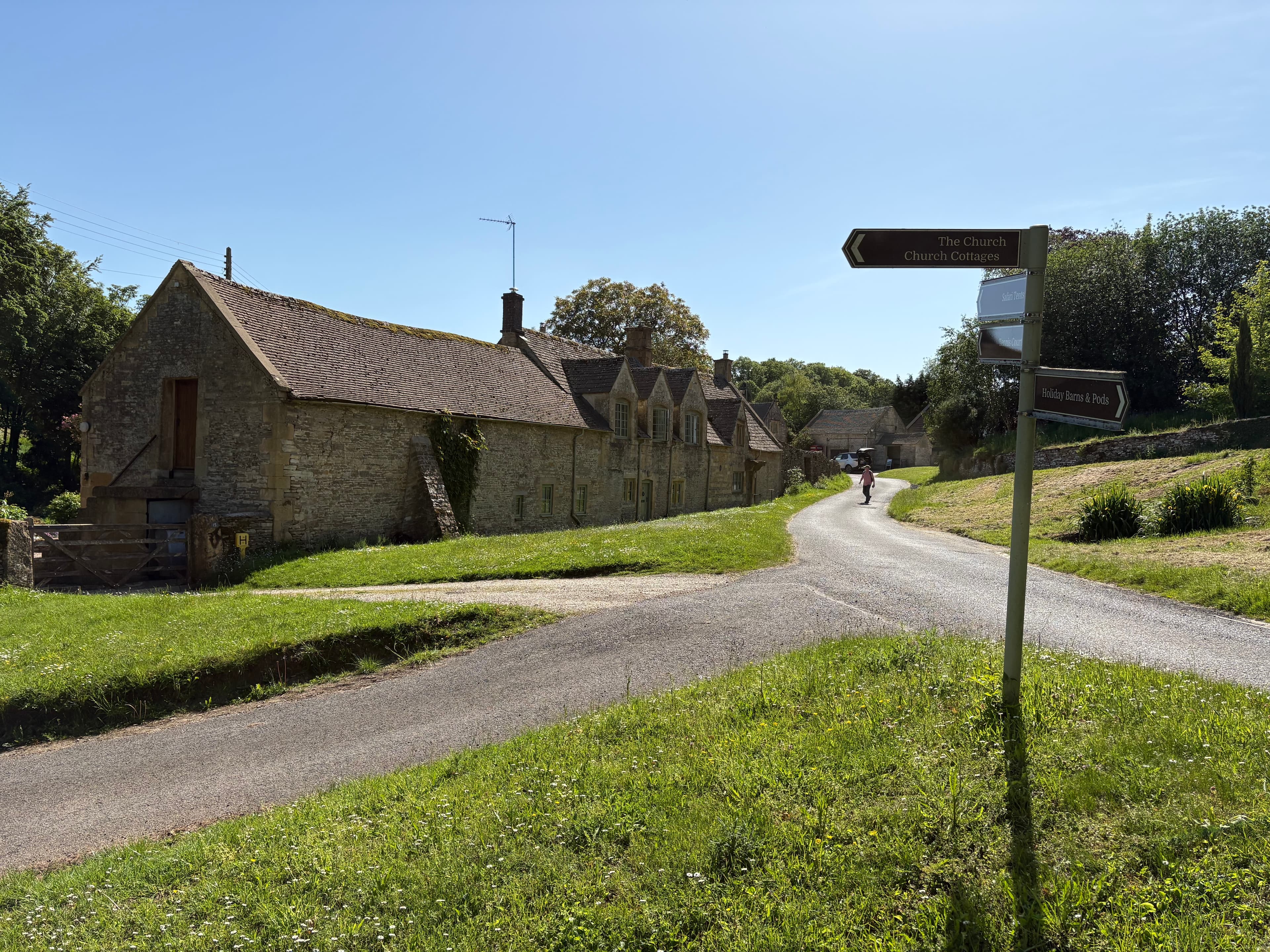 A stone barn and signposted lane through Notgrove, with a cyclist in the distance