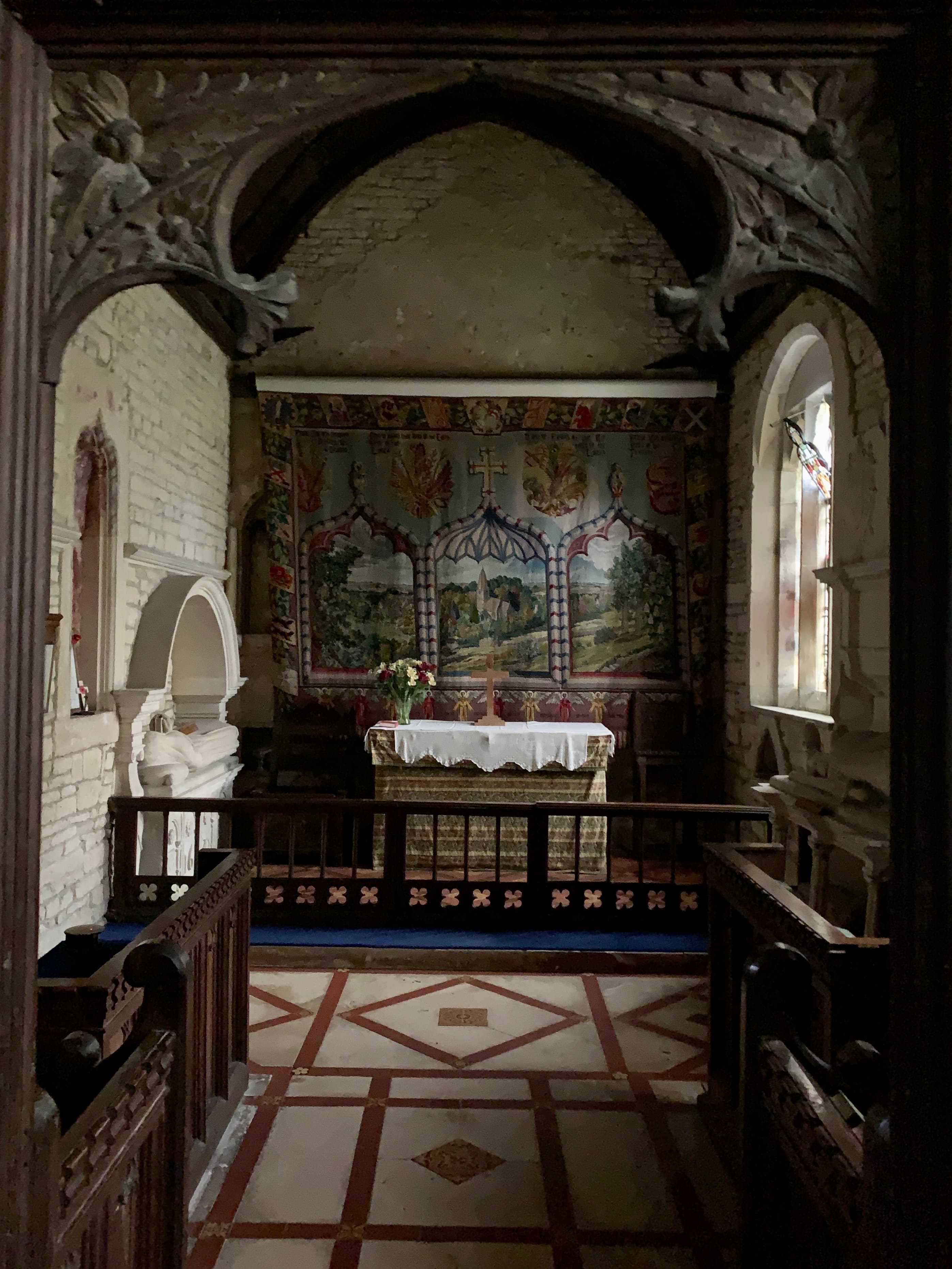 The chancel of St Bartholomew's, Notgrove — a painted reredos of landscape scenes within Gothic ogee arches above the altar