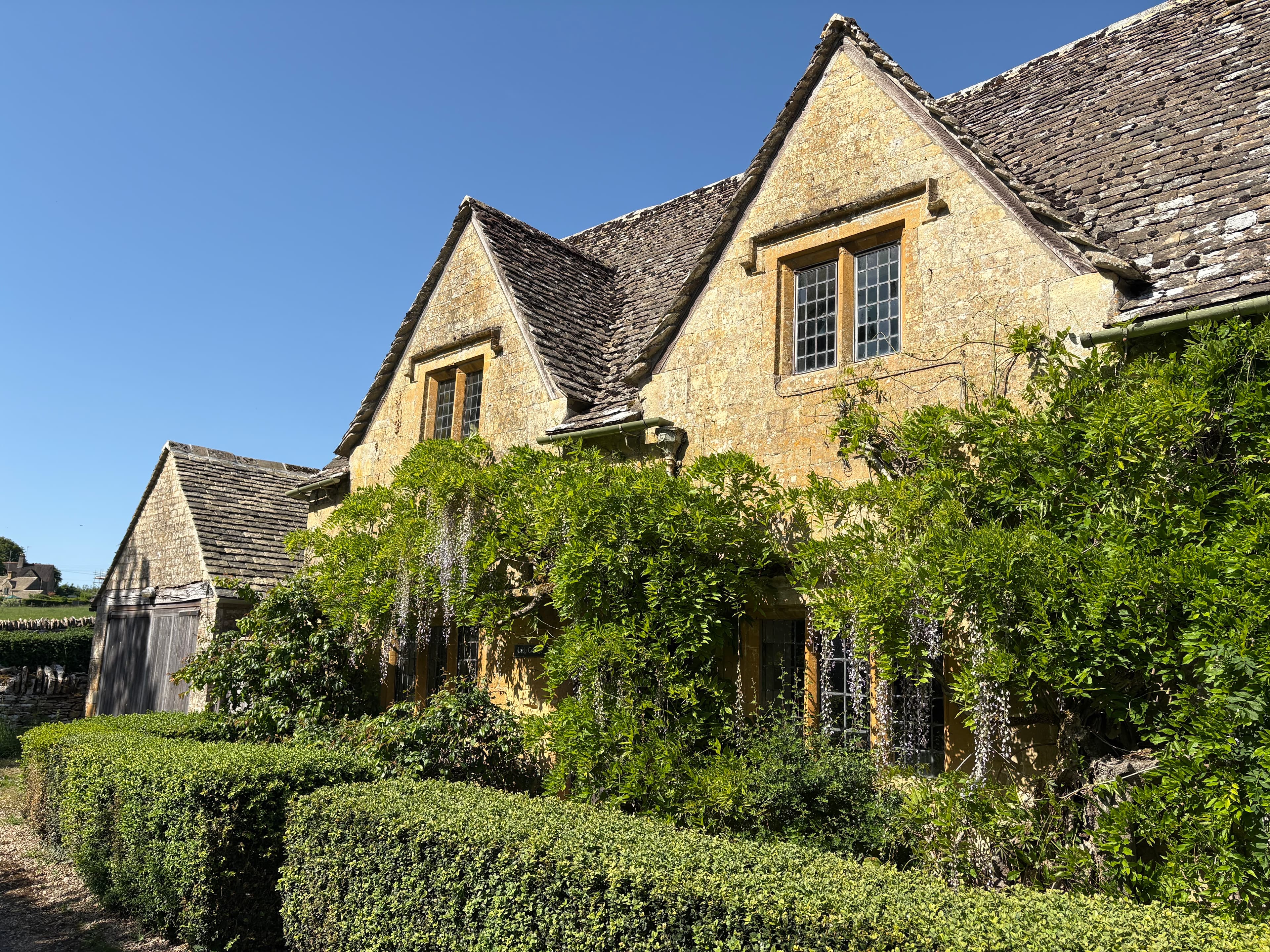 A honey-stone cottage at Notgrove draped in wisteria, low hedges in the foreground