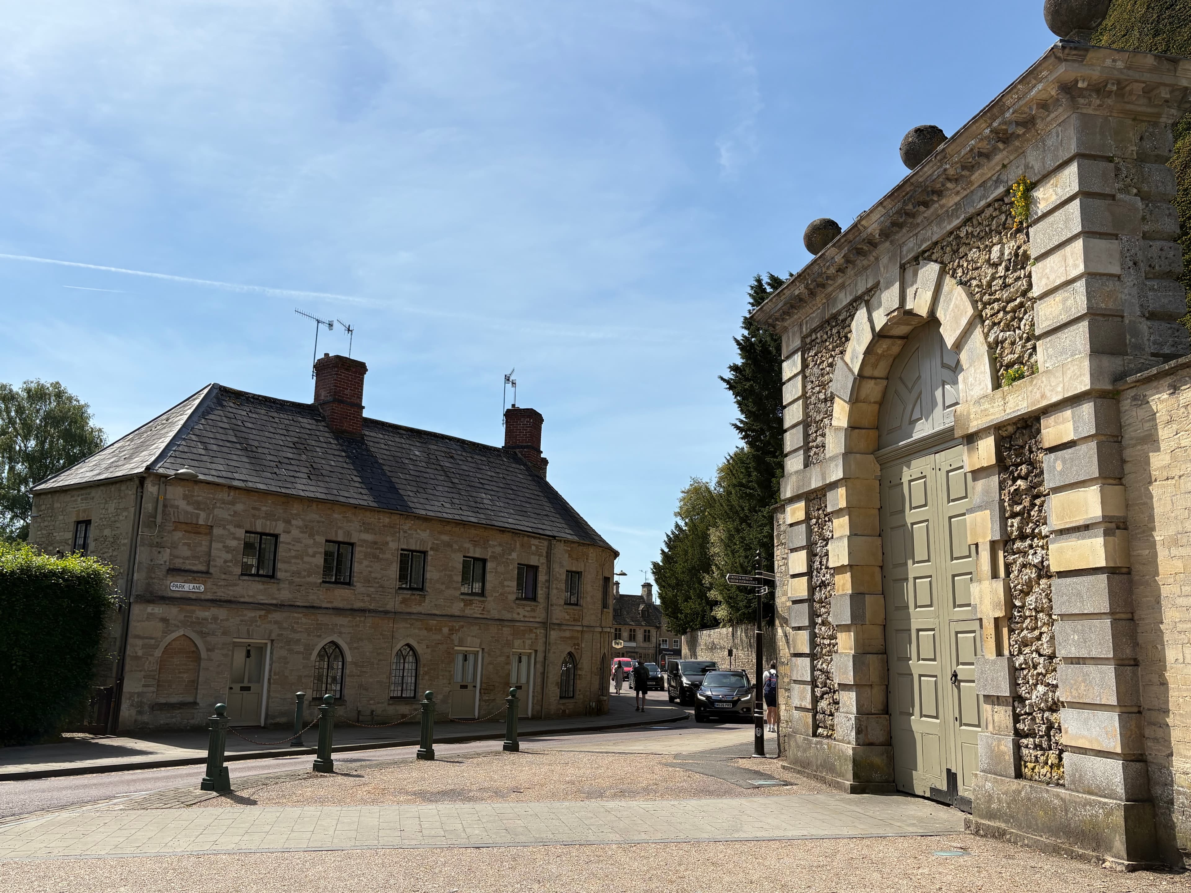 The Cirencester Park gate alongside the stone gatehouse building, on the corner of the high street