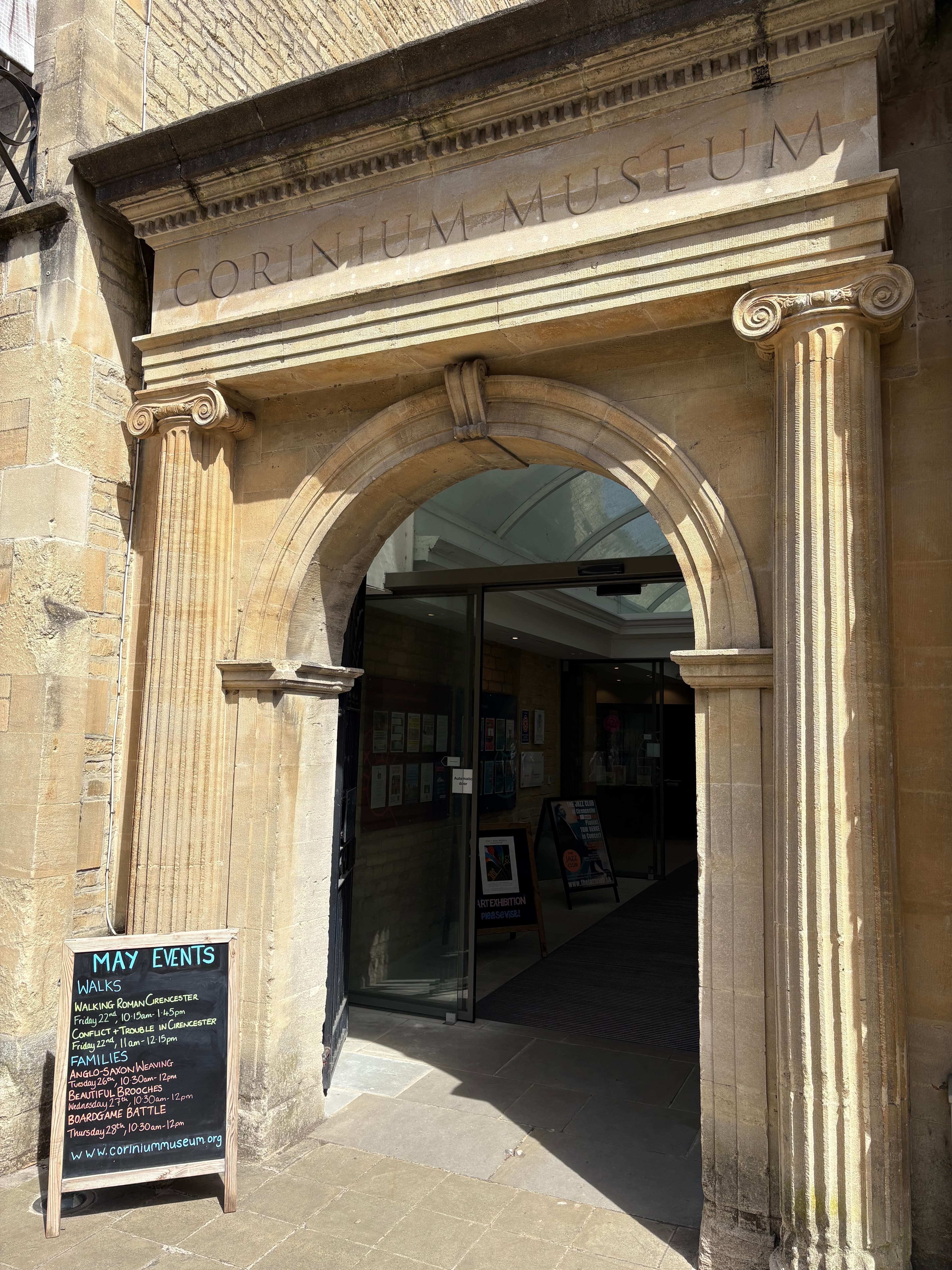 The arched stone entrance of the Corinium Museum, with 'CORINIUM MUSEUM' carved above the doorway and Ionic columns either side