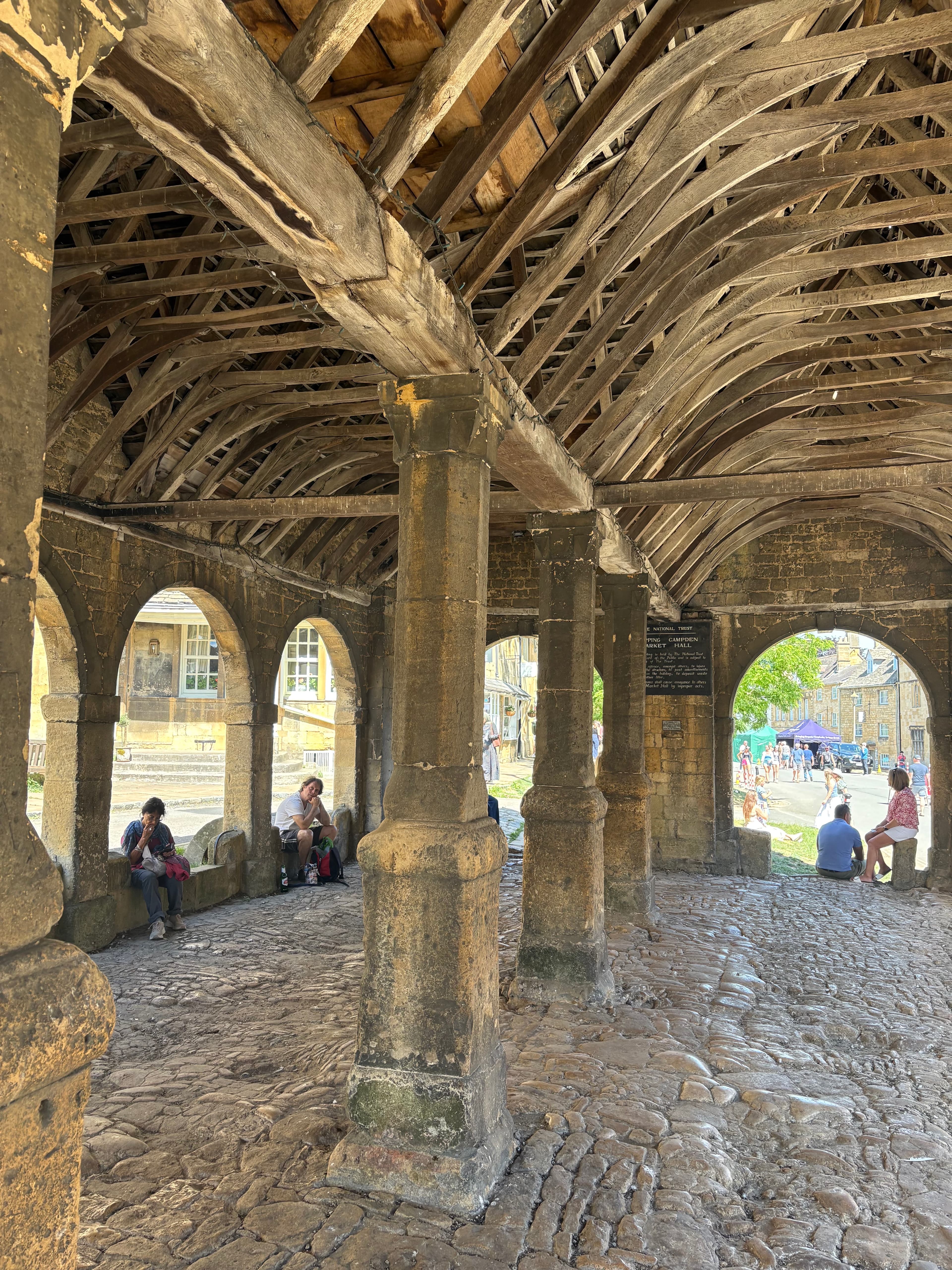 Inside the Market Hall — stone pillars, exposed roof timbers and view through the arches to the village