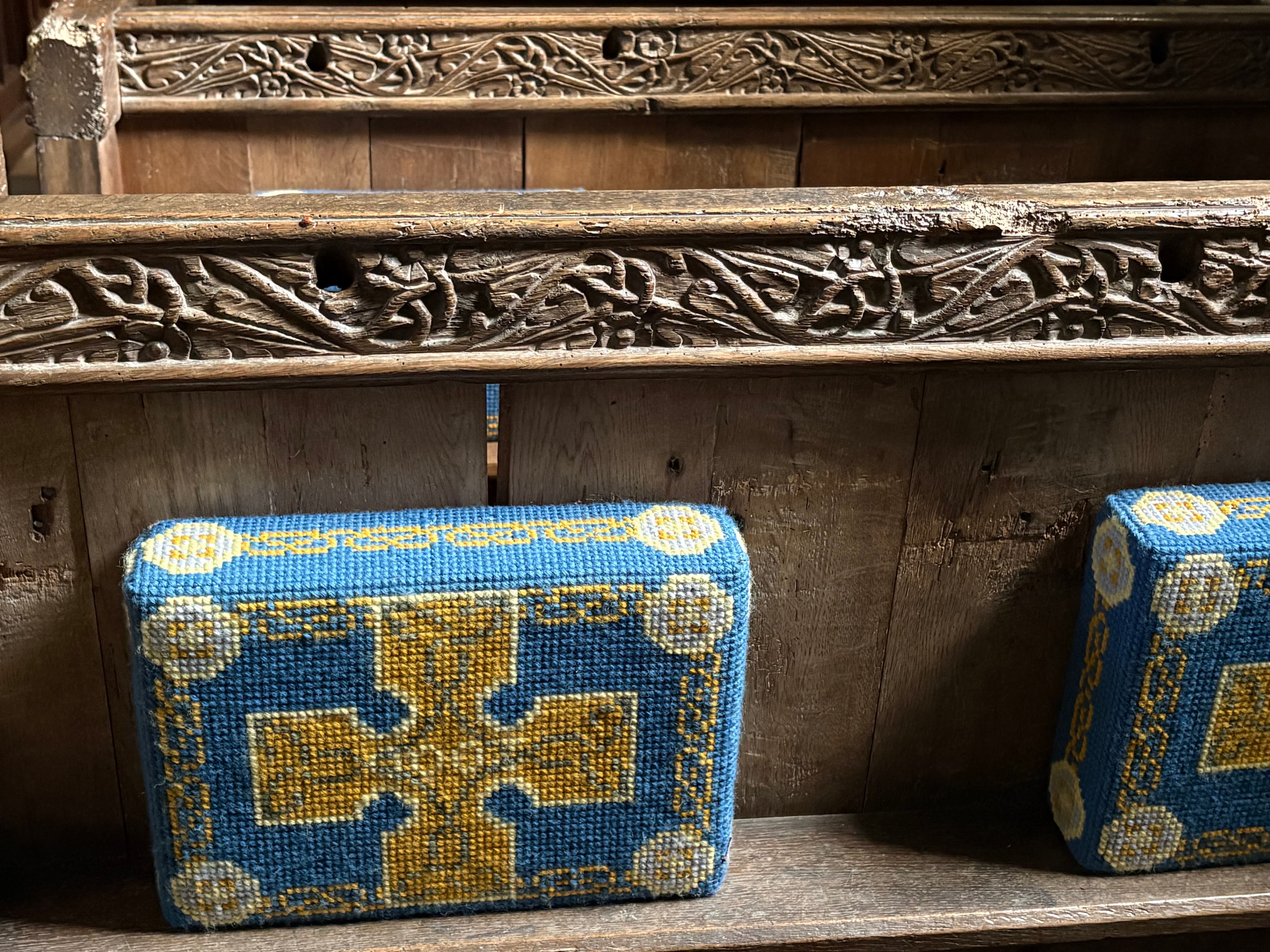 Detail of one of the 16th-century carved oak benches at St Bartholomew's, with a blue-and-yellow embroidered kneeler in front