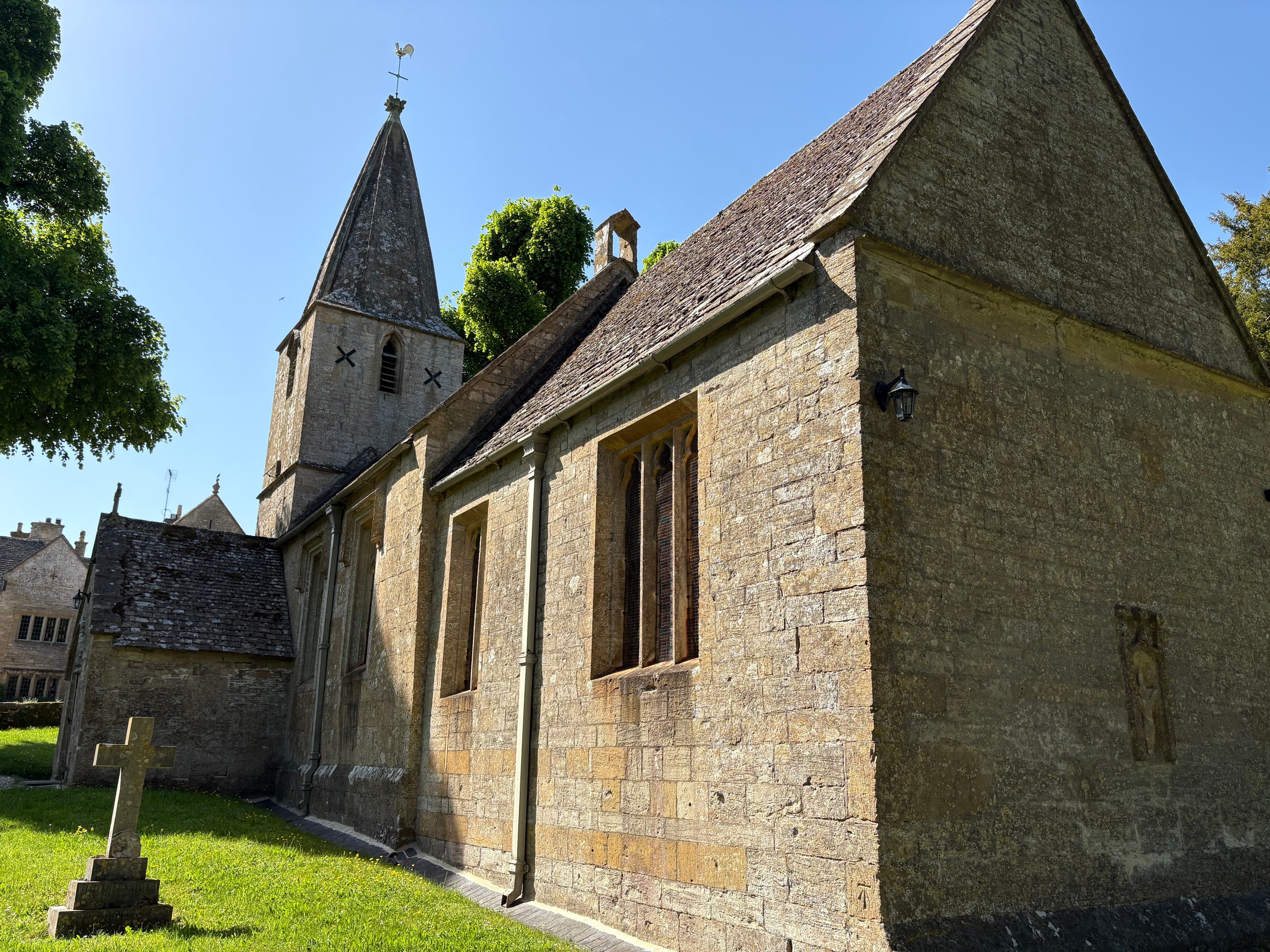 Side view of St Bartholomew's, Notgrove — tower, short spire and nave seen across the churchyard