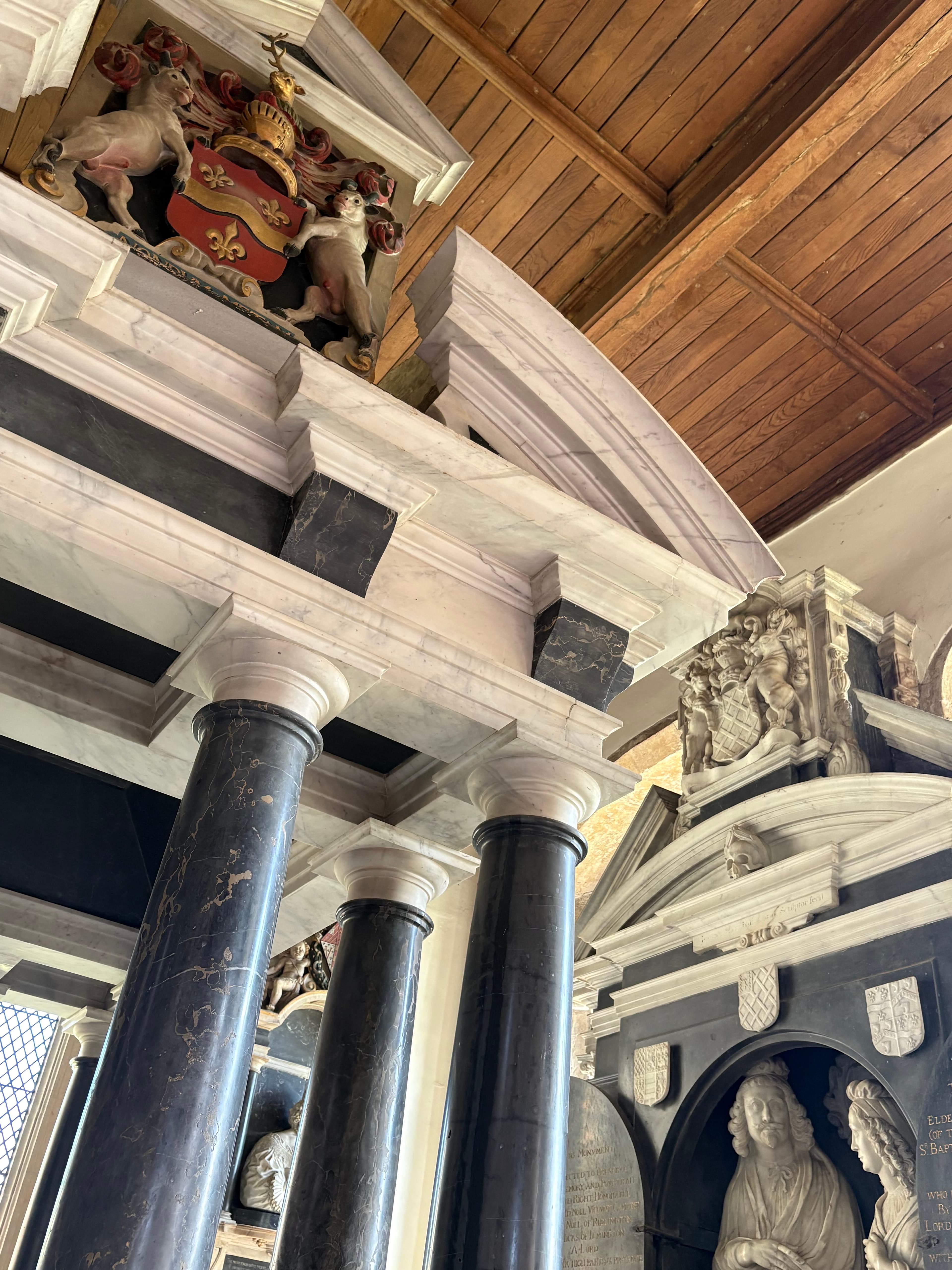 Detail of the Hicks family tomb monument at St James's — black marble columns, painted heraldry and a carved cherub