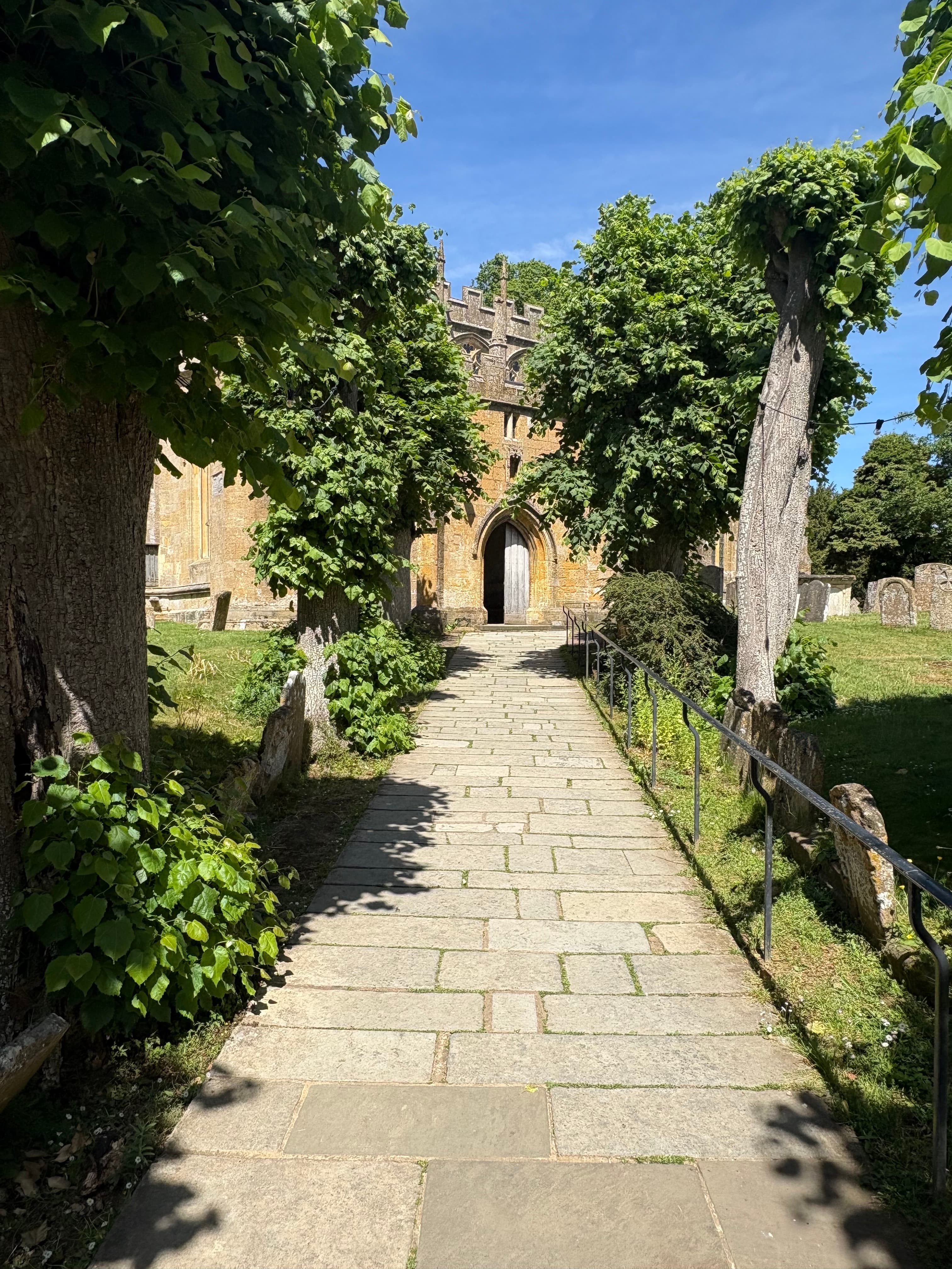The yew-lined avenue leading to the church door, with low evening light along the path