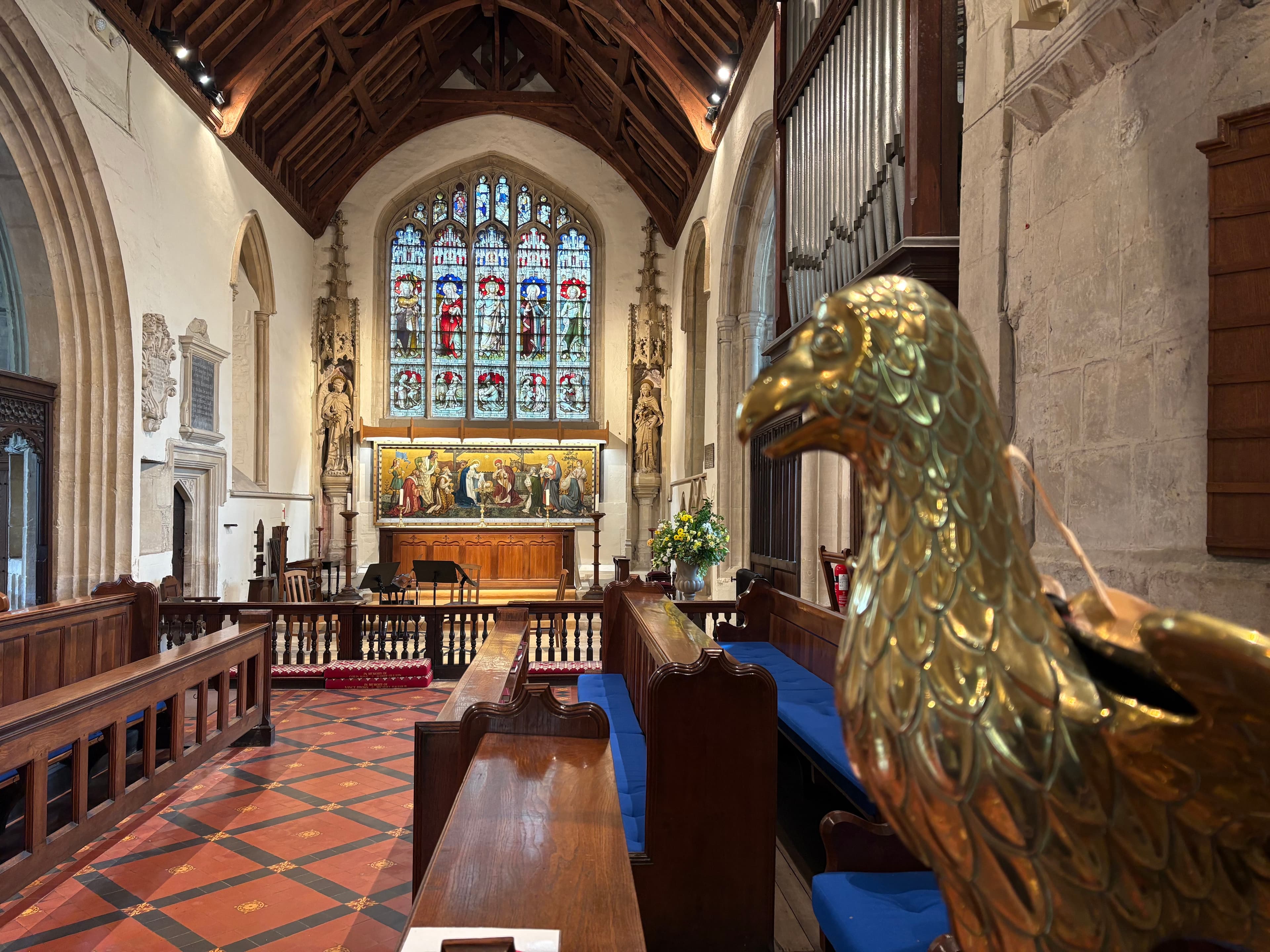 Looking down the chancel — east window, painted reredos, and a brass eagle lectern
