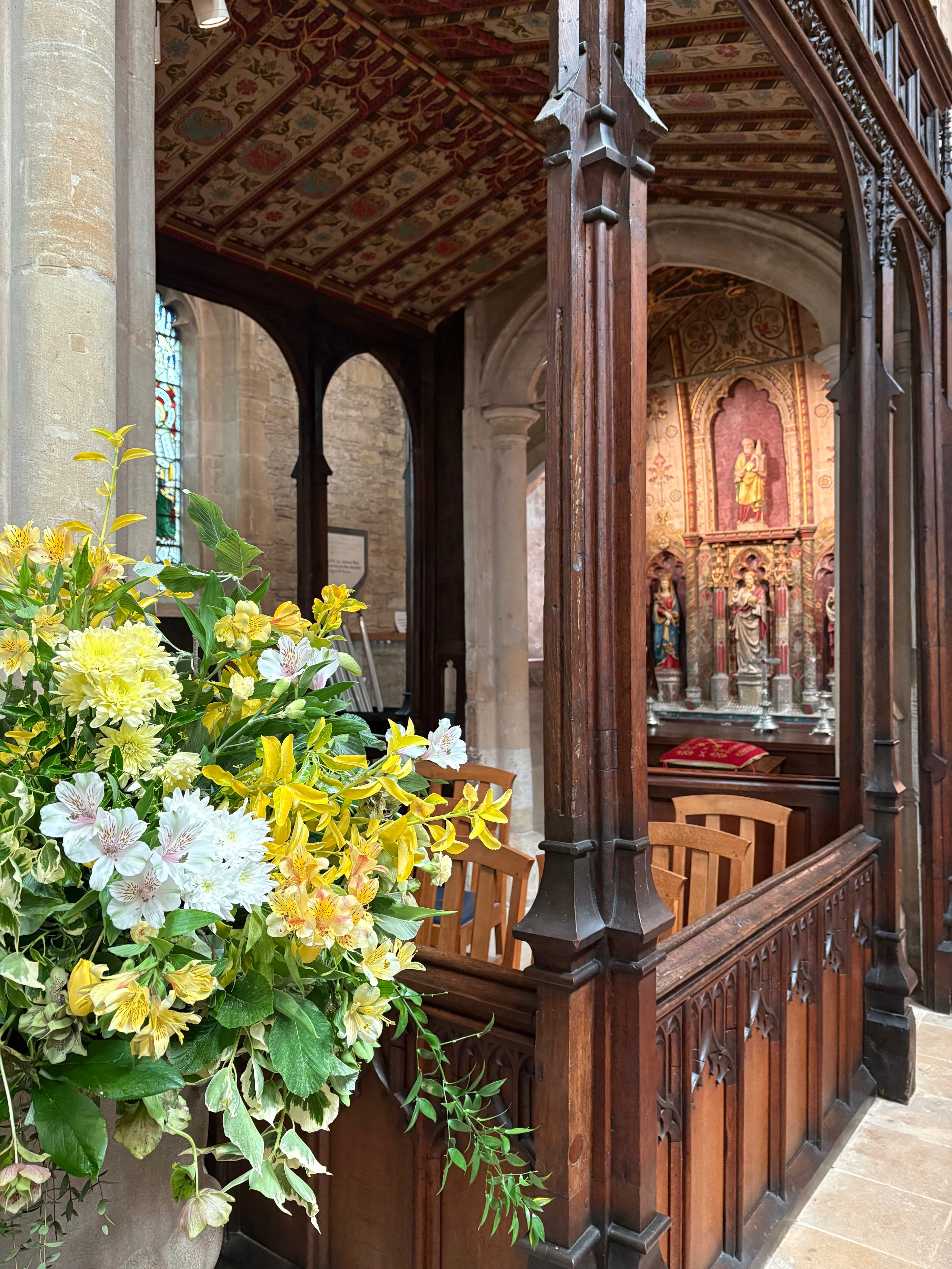 A wooden Perpendicular screen with a vase of flowers and the chancel beyond