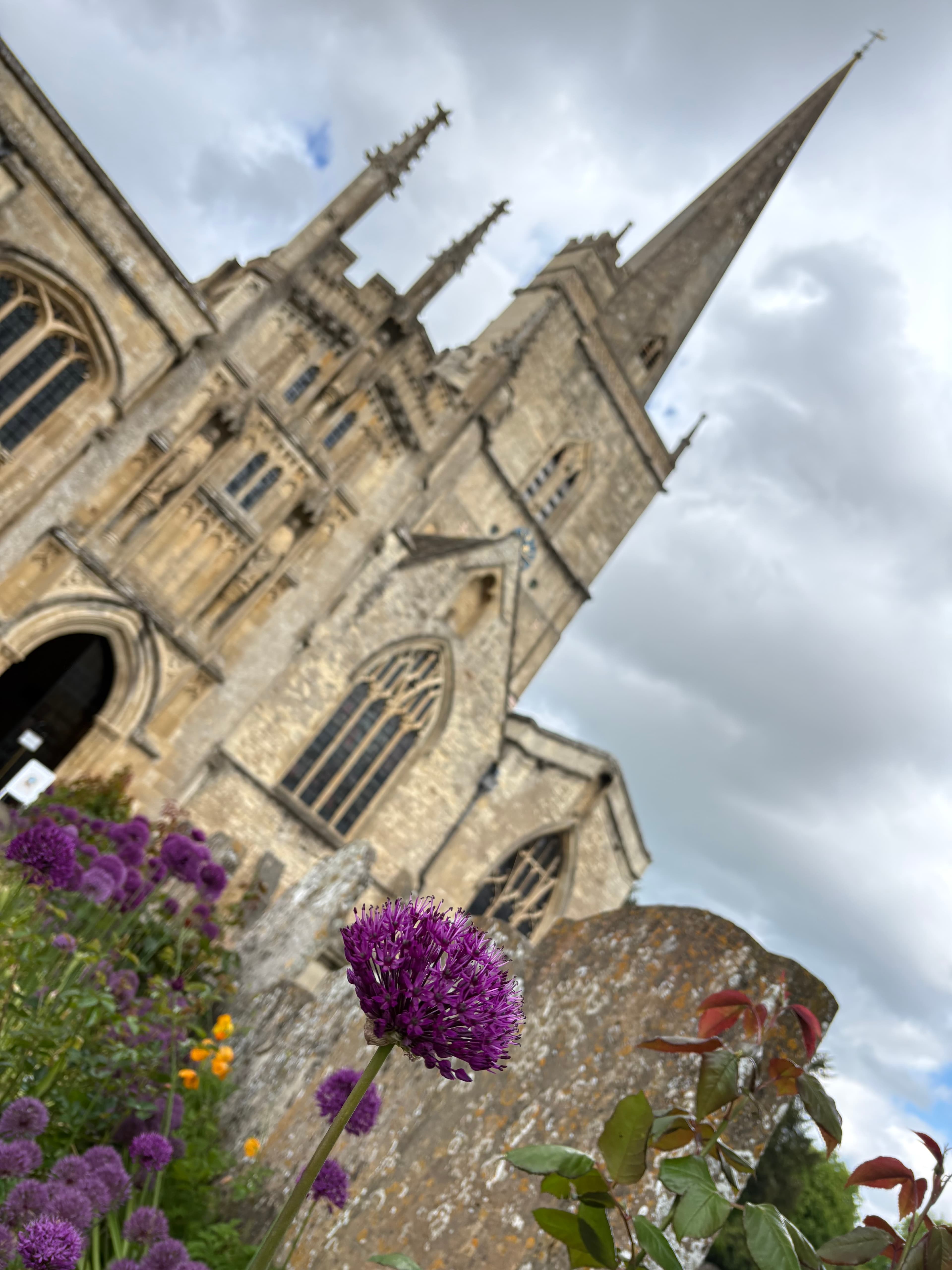 St John the Baptist, Burford — the spire rising above the churchyard, alliums in the foreground