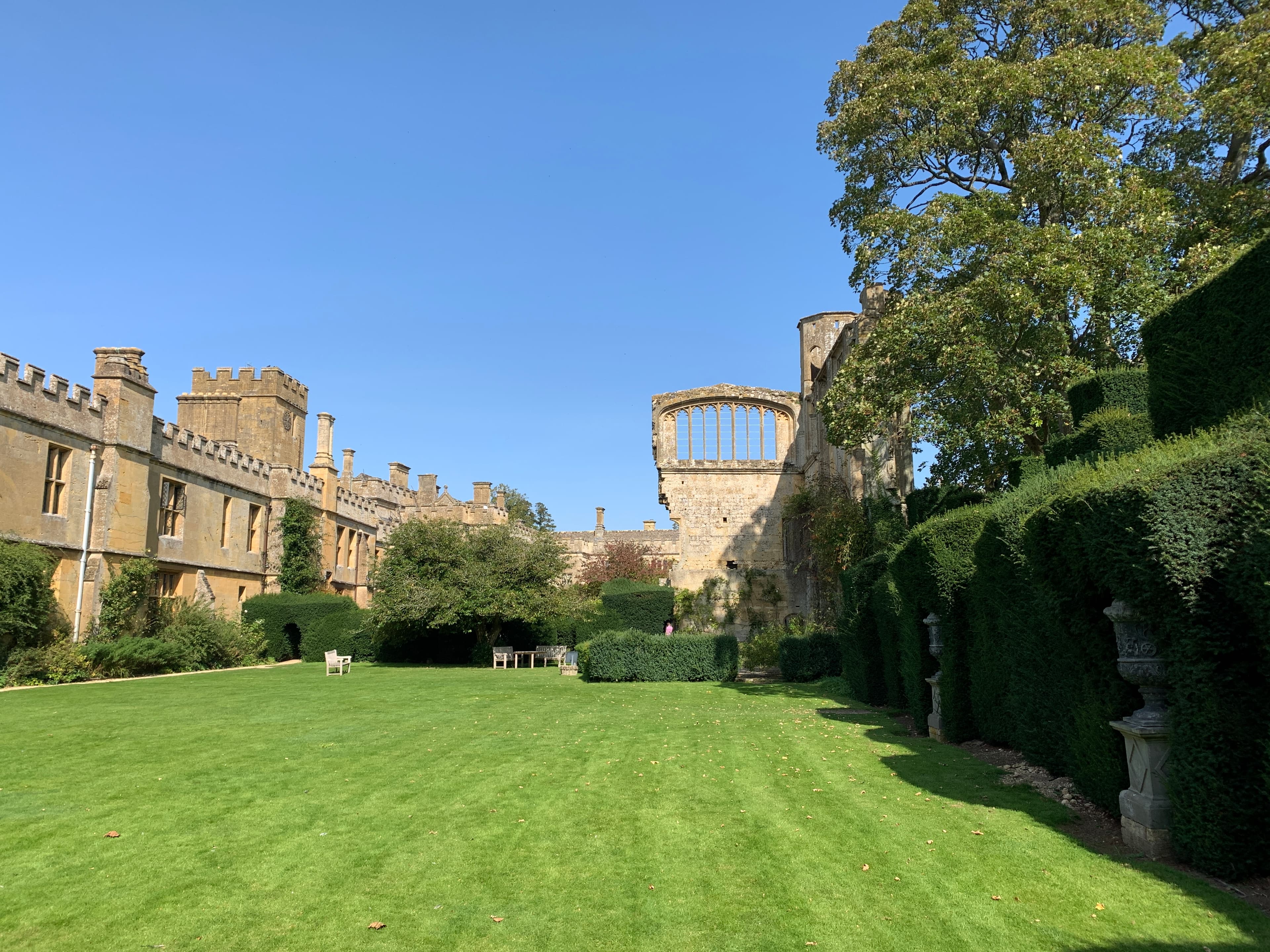 Sudeley's east wing and the ruined arches of the medieval Tithe Barn, with a yew topiary hedge on the right