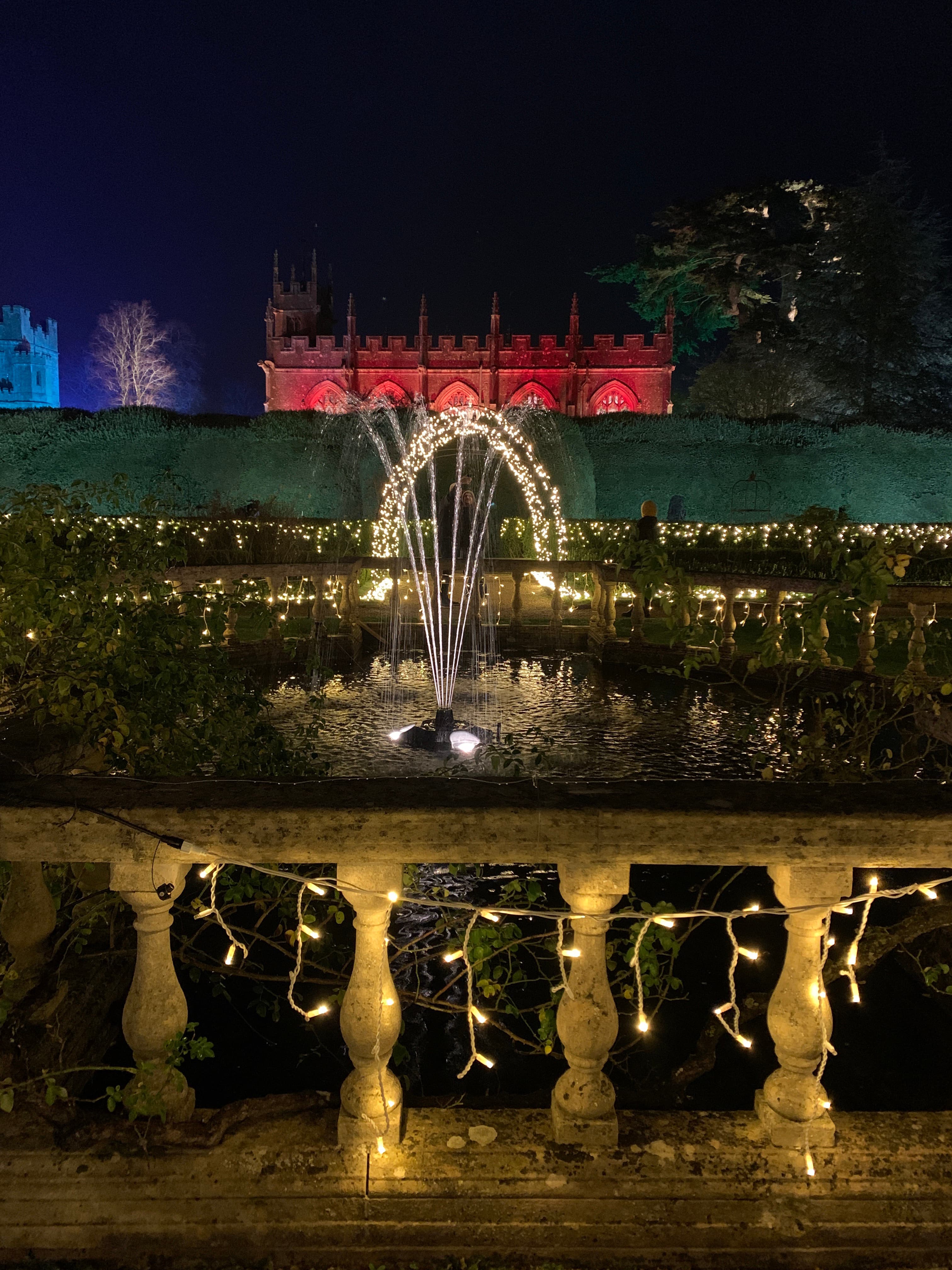 An illuminated dandelion-style light fountain on a Sudeley lawn, with the castle silhouette and chapel beyond