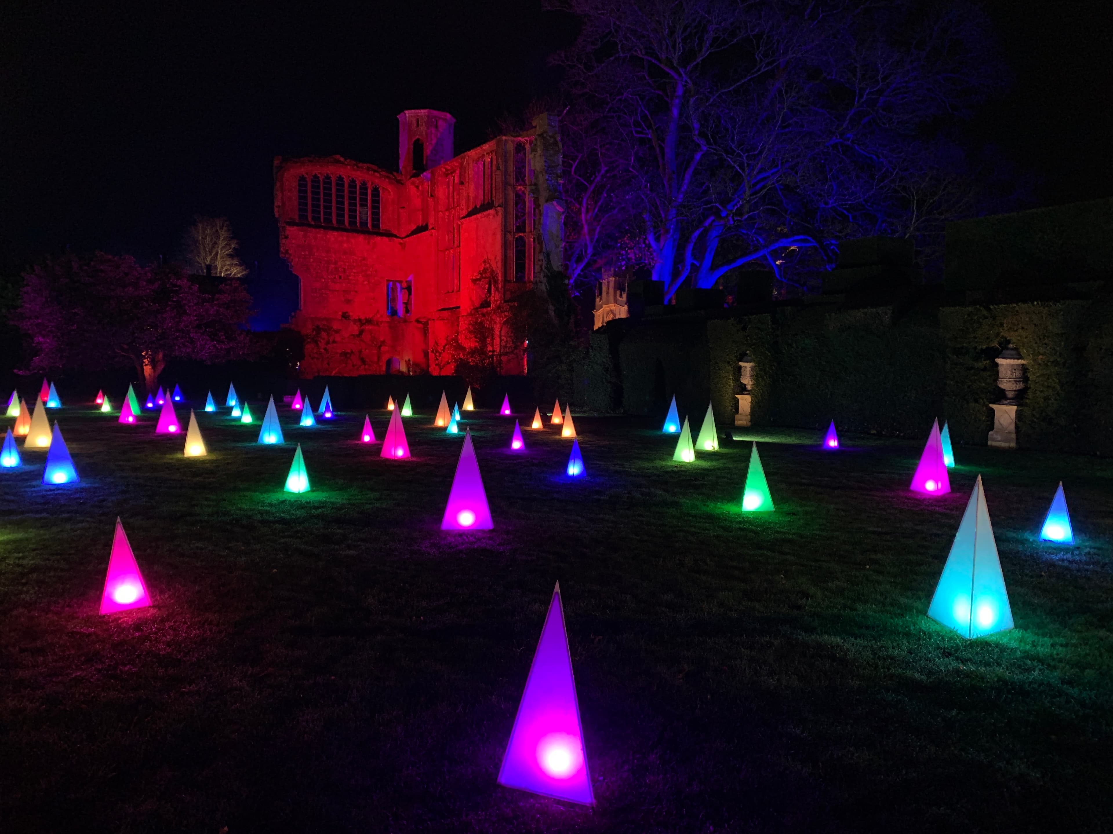 A field of multicoloured LED pyramids on the lawn beside the ruined Tithe Barn at Sudeley, lit for the winter Spectacle of Light