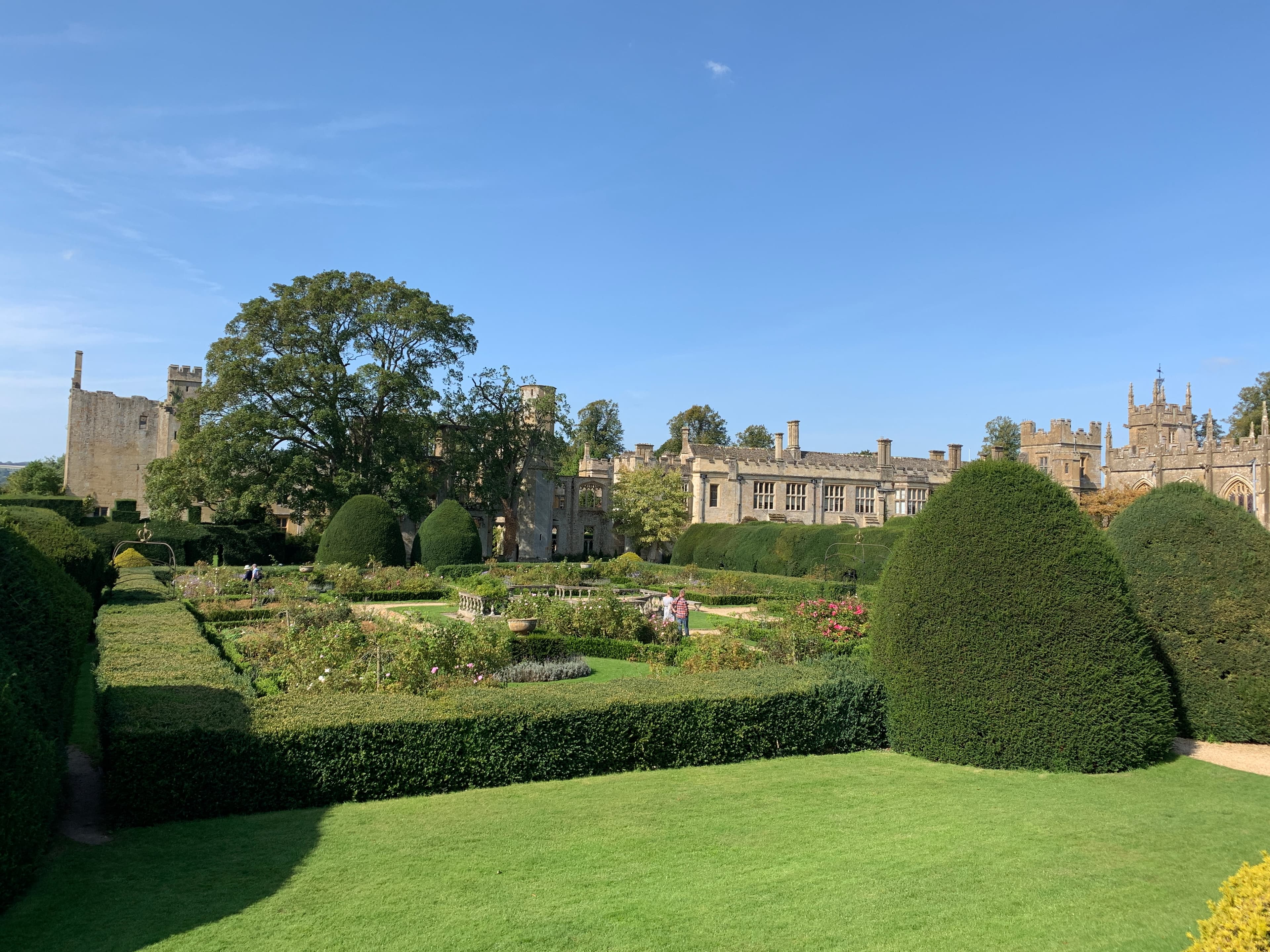 Sudeley's Queen's Garden — formal parterre, topiary cones and rose beds in front of the castle's main range, with the chapel tower beyond