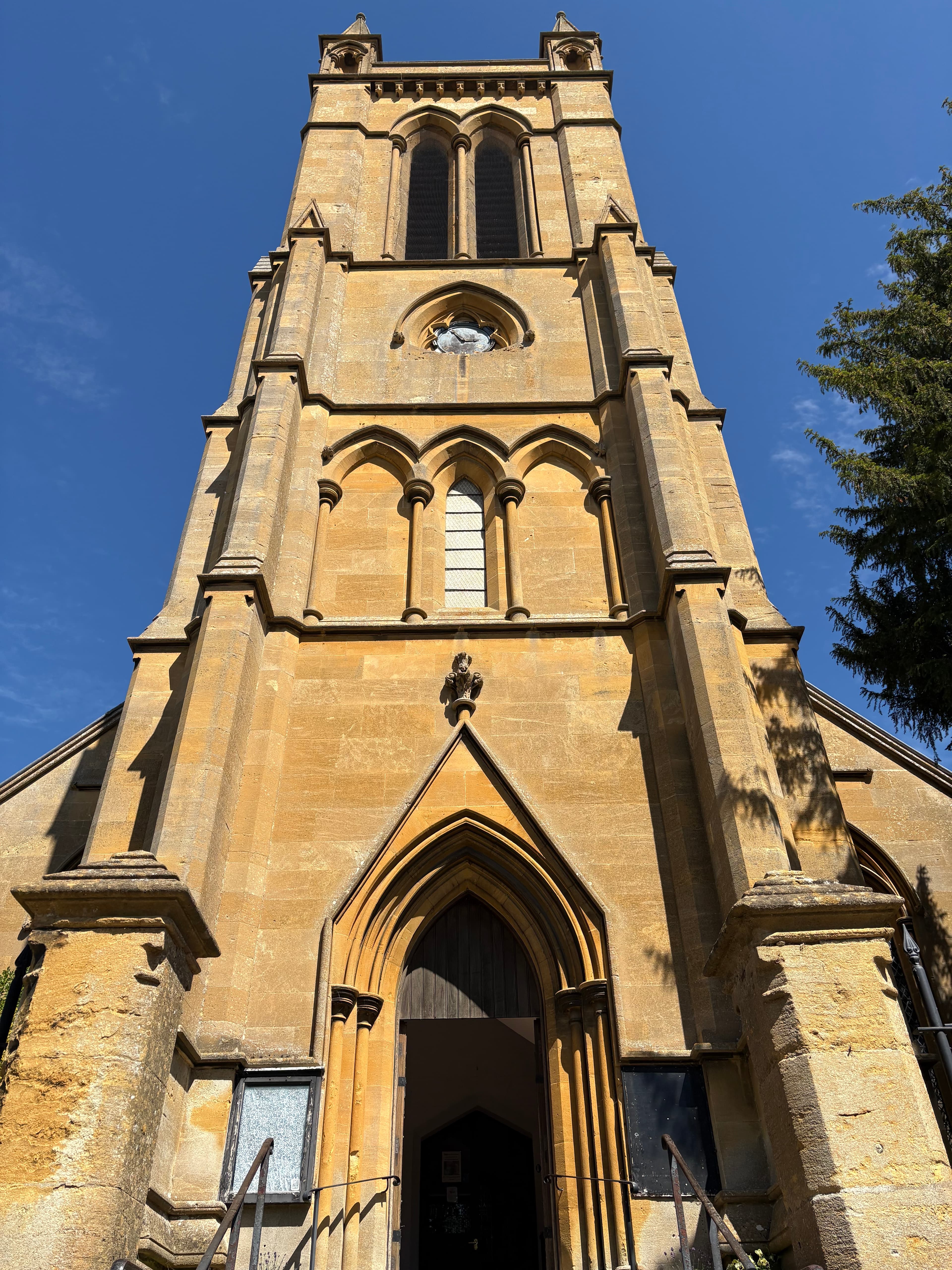 Looking up at the tower of Broadway's parish church — sandstone with tall traceried windows