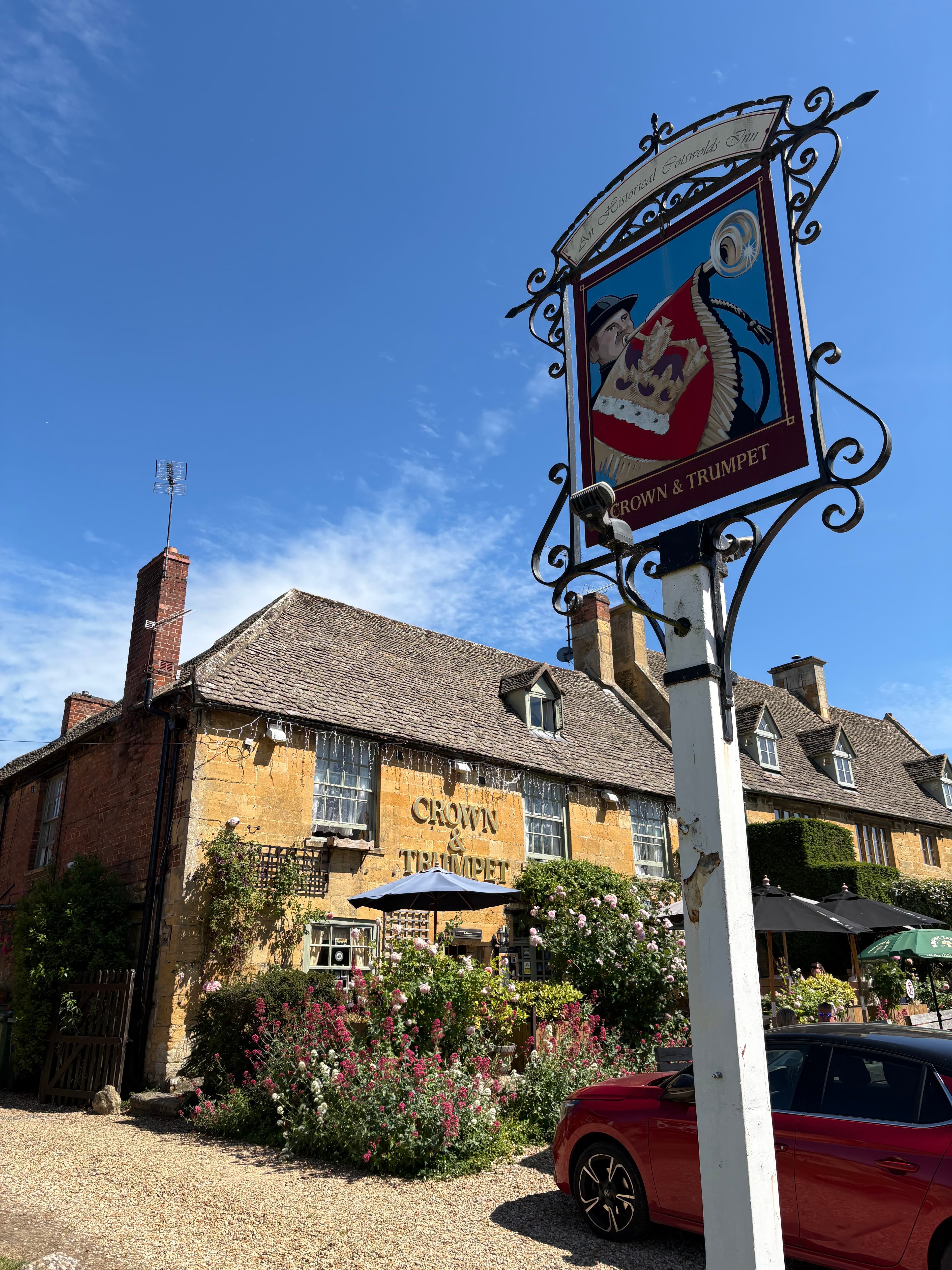 The wrought-iron sign of the Crown & Trumpet pub, with the inn behind