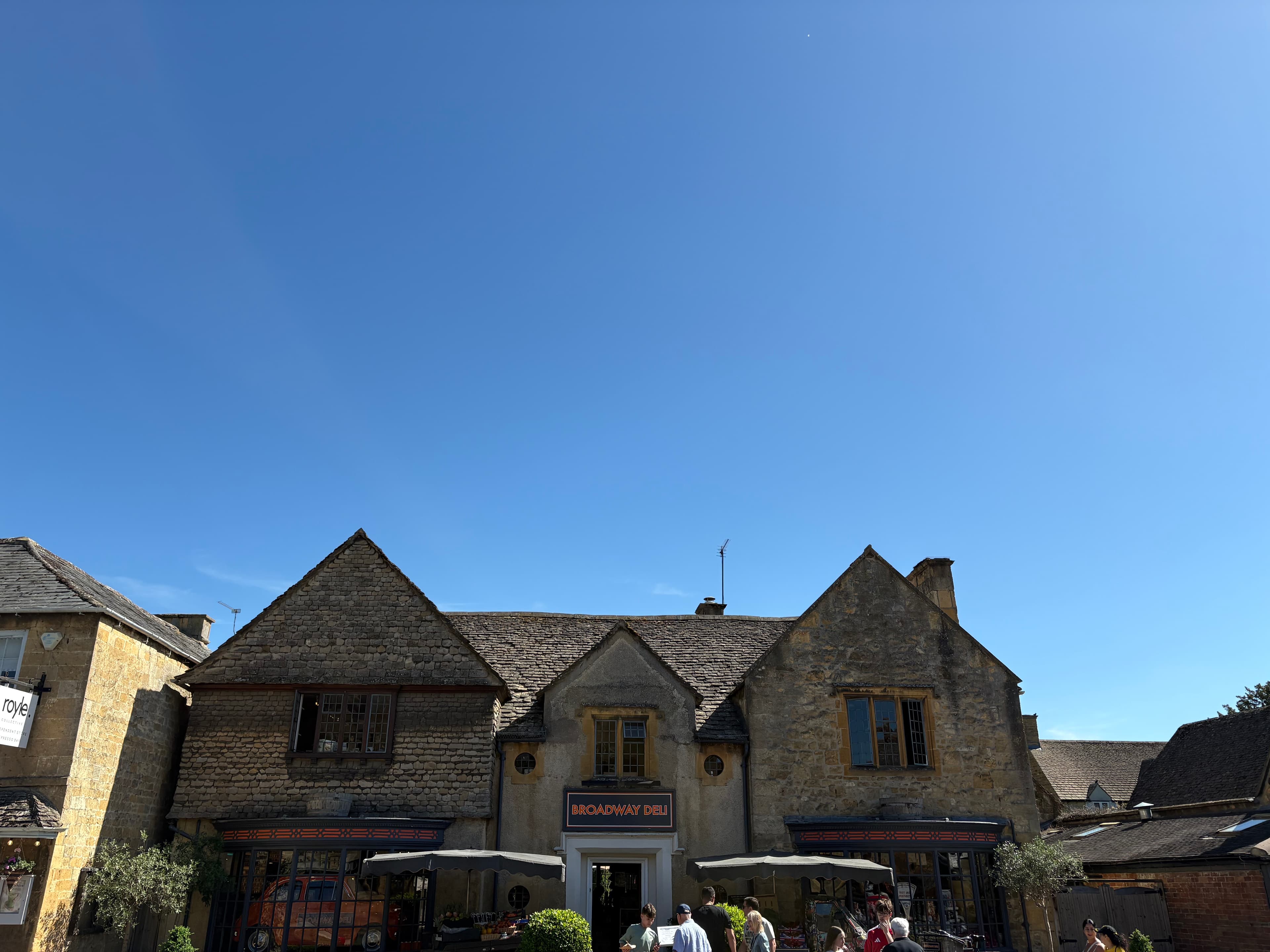 Broadway Deli — a gabled Cotswold-stone building set behind a small square of pavement cafés