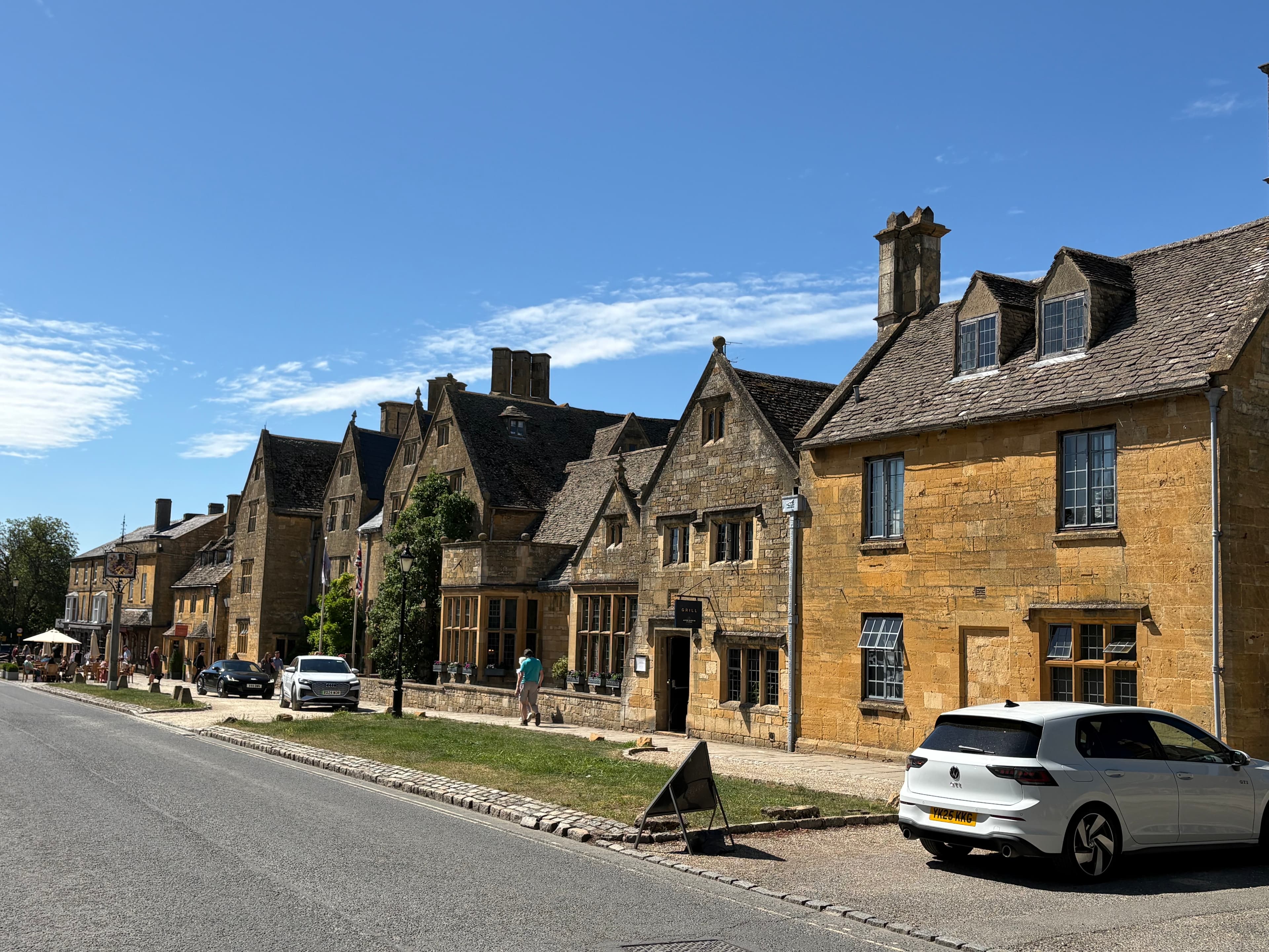 A row of honey-stone gabled cottages along Broadway's high street under a clear blue sky
