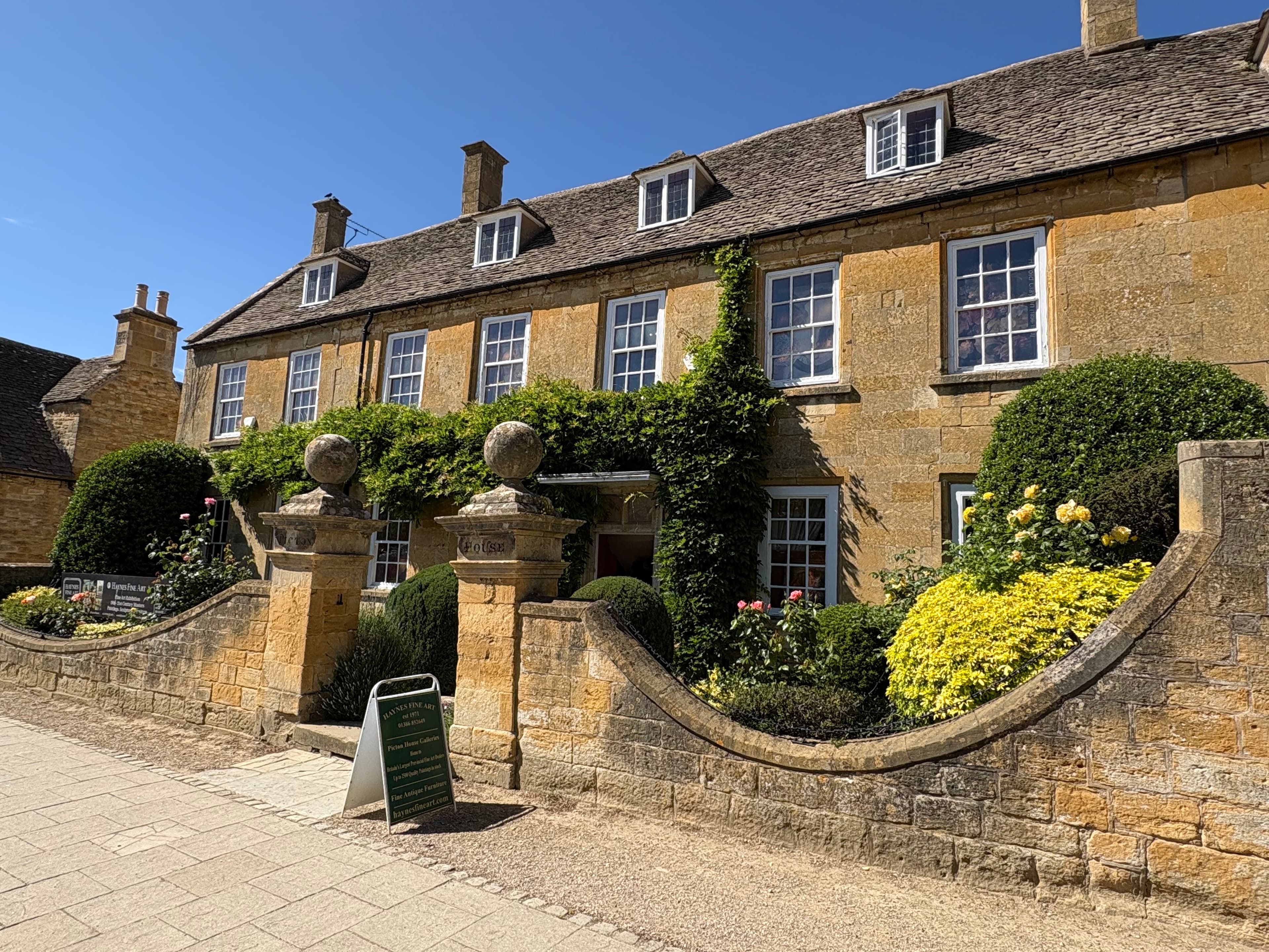 A Cotswold-stone inn on Broadway's high street with topiary balls flanking a stone-pillared gate