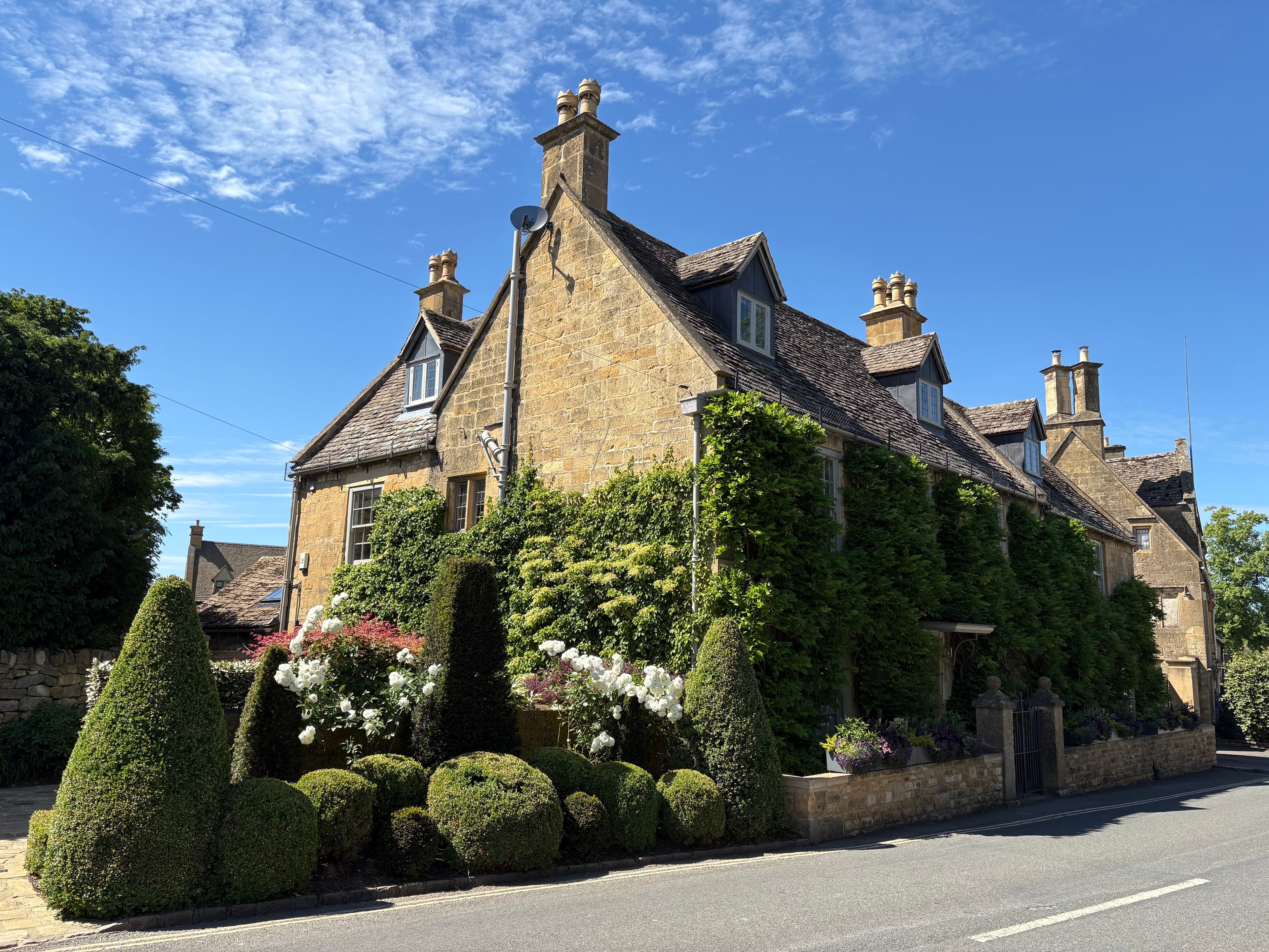A Cotswold-stone house in Broadway with Virginia creeper and a row of conical topiary along the front garden