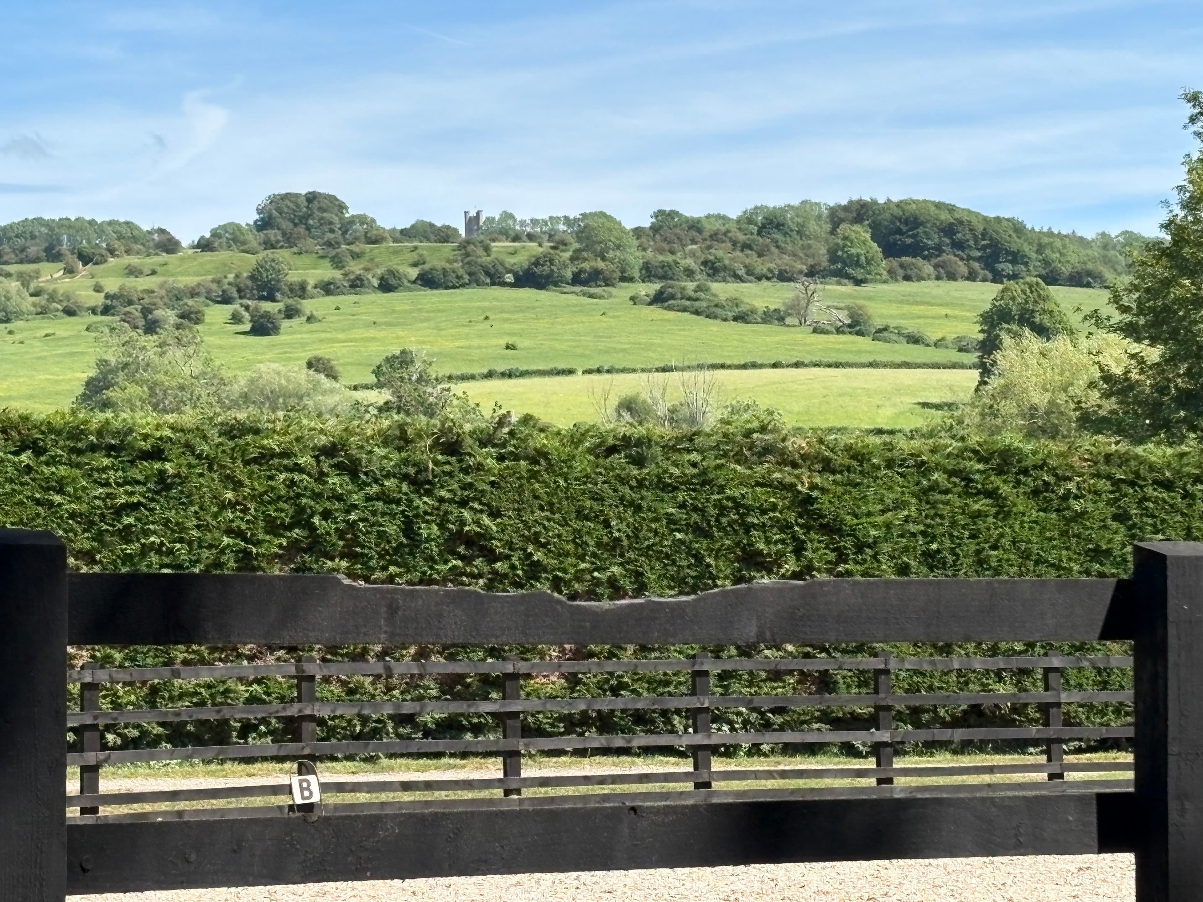 Broadway Tower seen on the hilltop above the village, framed by a wooden gate and hedge in the foreground