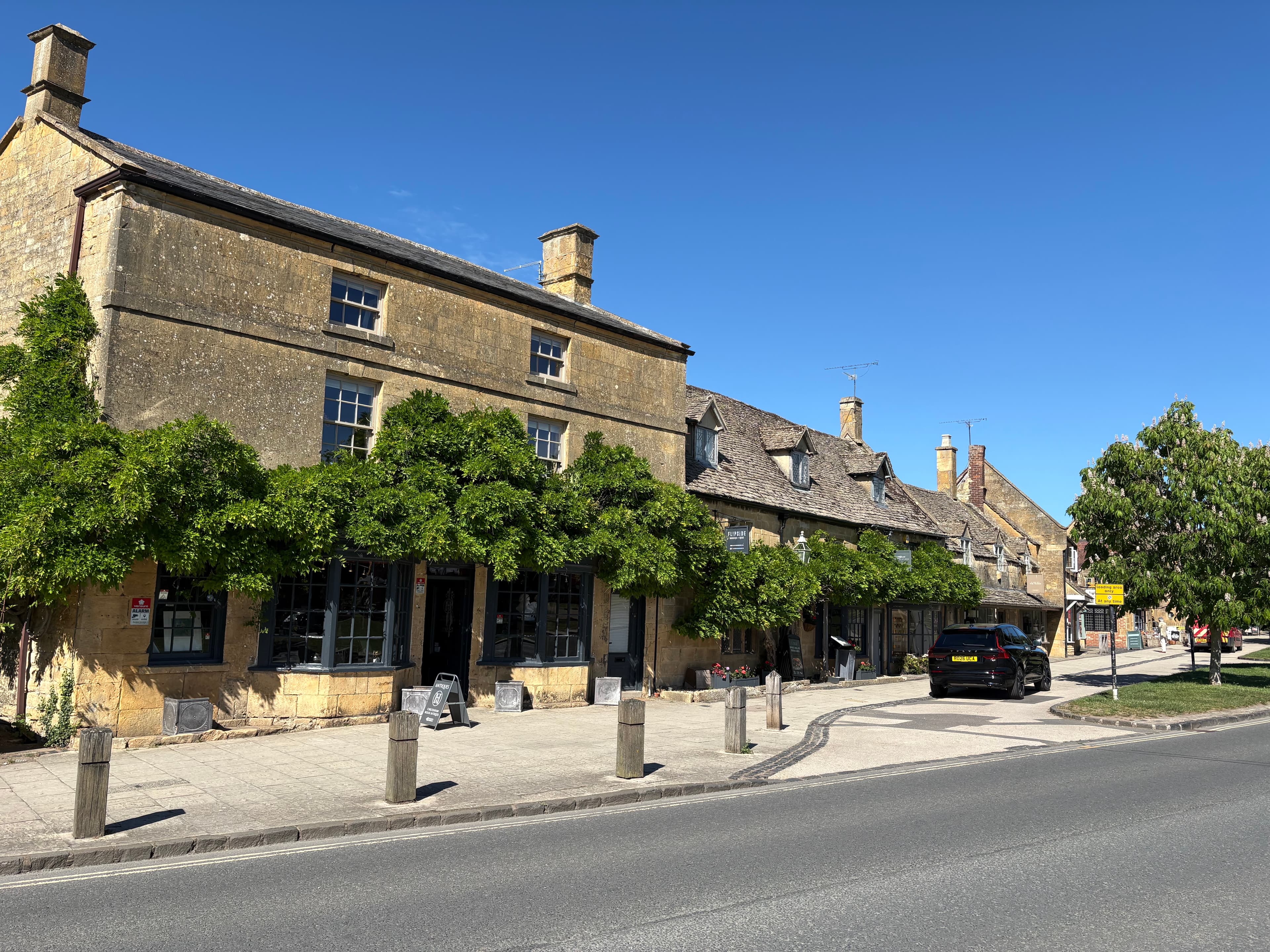 A row of Broadway shops shaded by lime trees on the high street