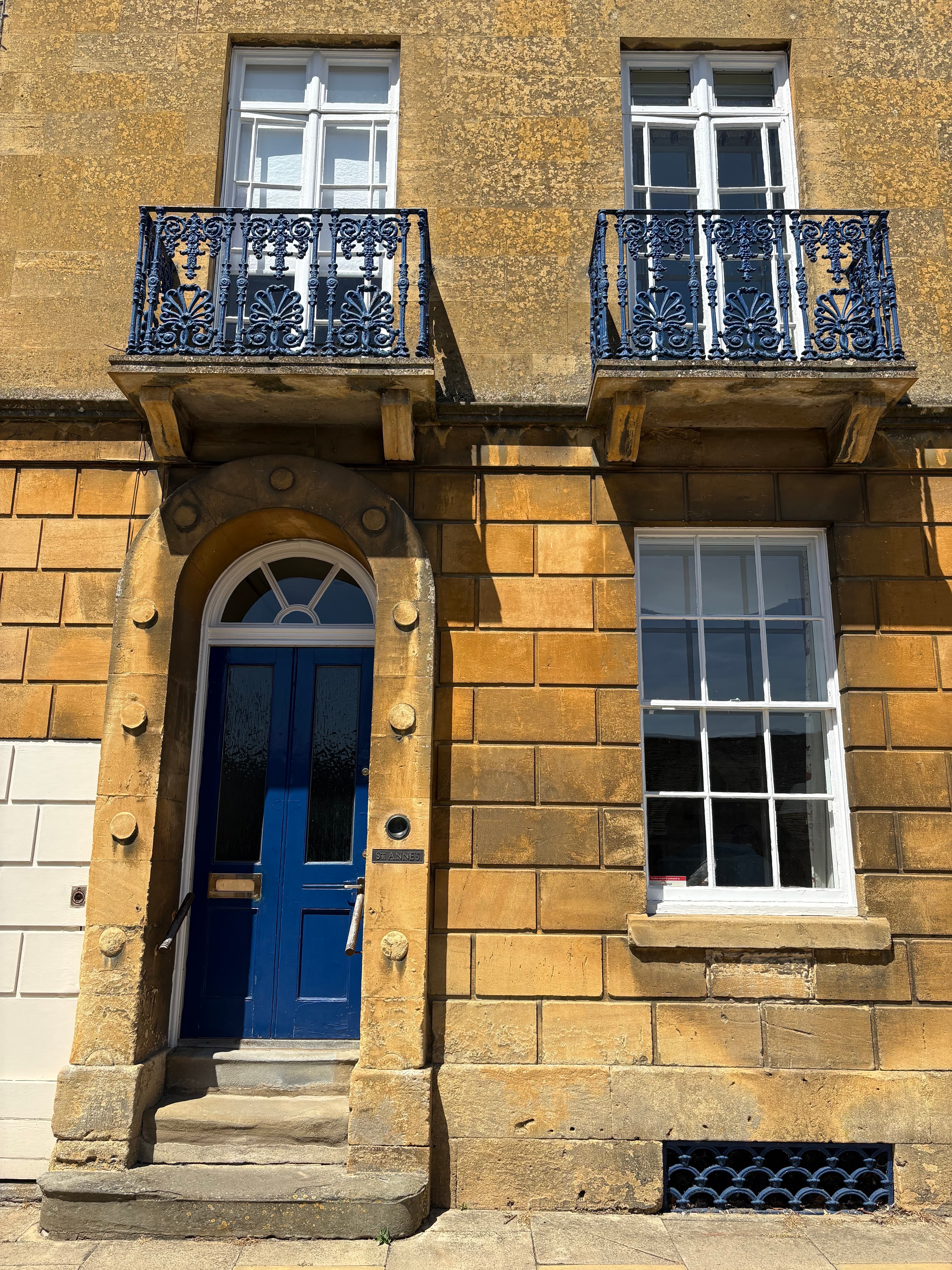 A blue-painted Georgian front door with arched fanlight, set between sash windows with iron balconies
