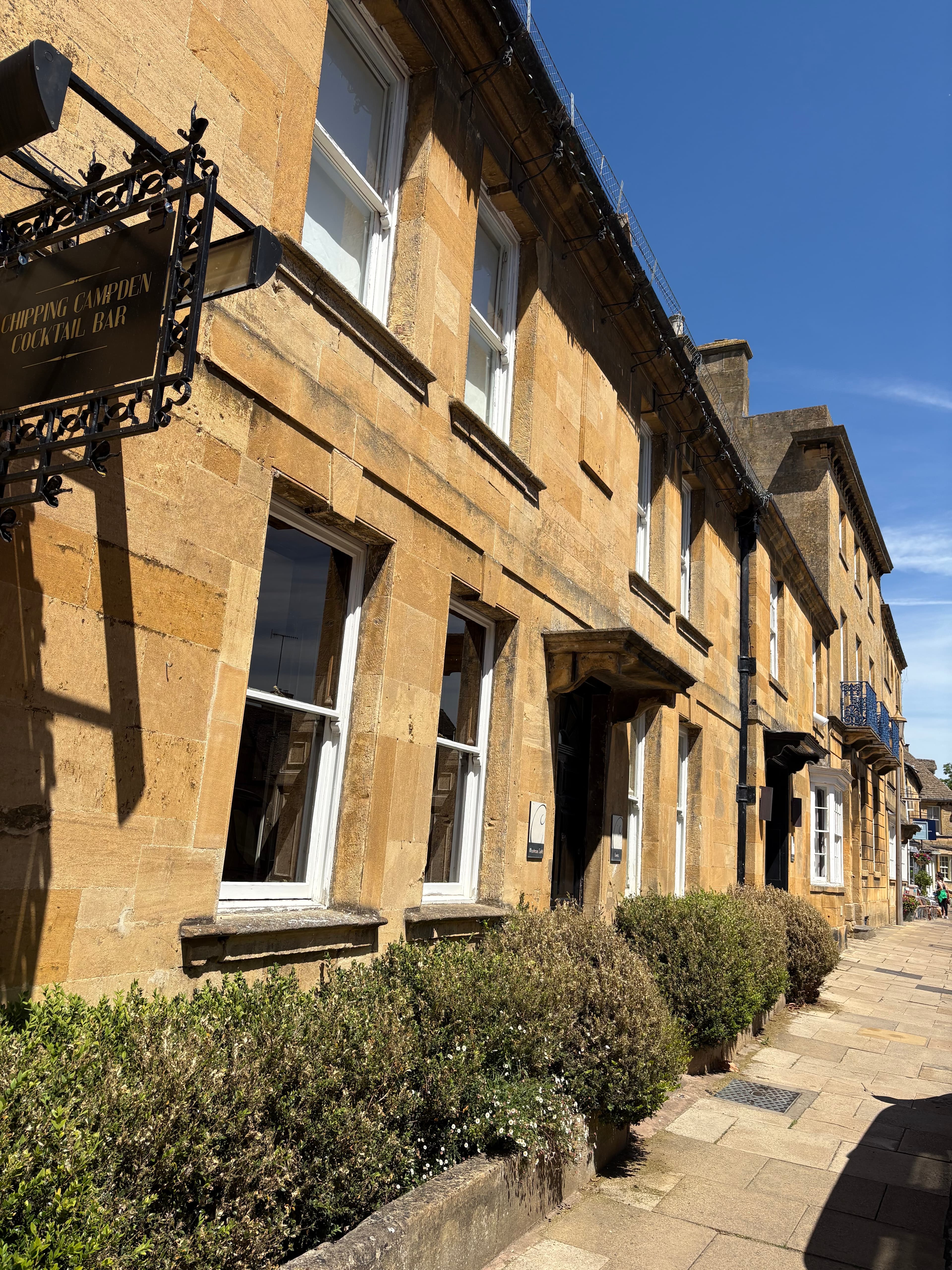Looking up the tall Cotswold-stone facade of a High Street townhouse, sash windows ranged across multiple storeys