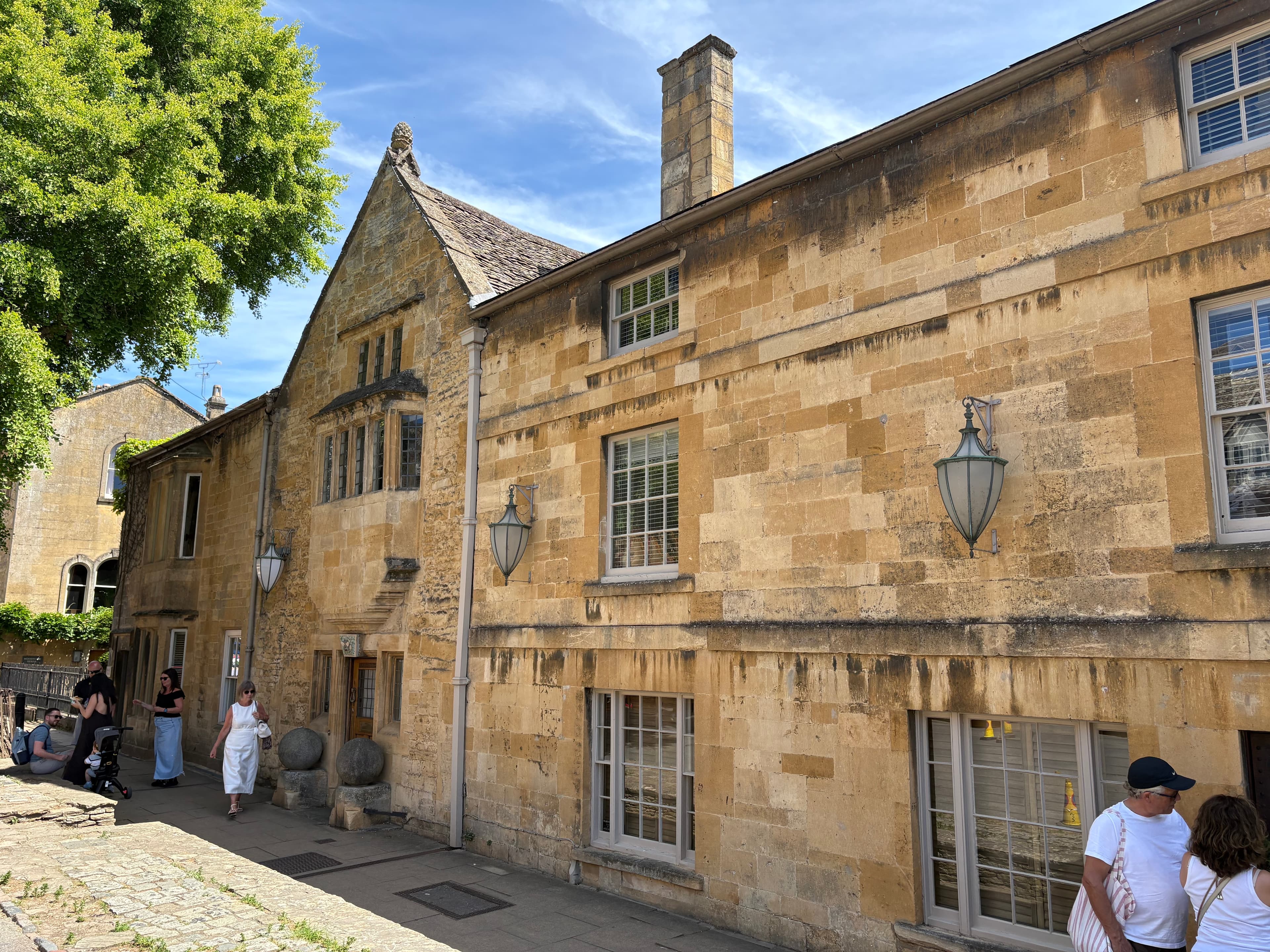 Honey-stone gabled buildings along the High Street with visitors strolling on a summer afternoon