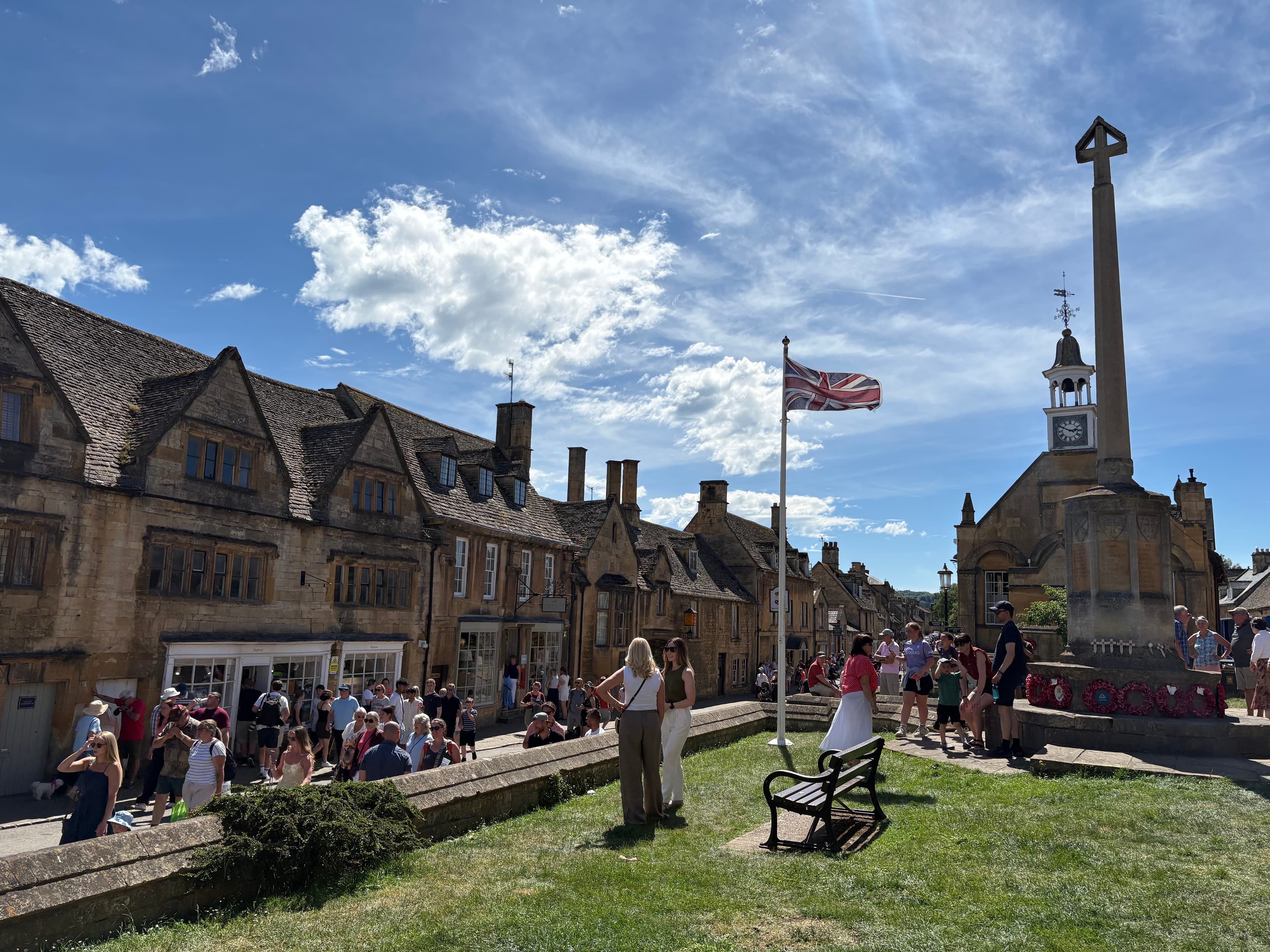 A sunny summer afternoon on the High Street with the Market Hall, war memorial cross and a Union Jack flying over the village