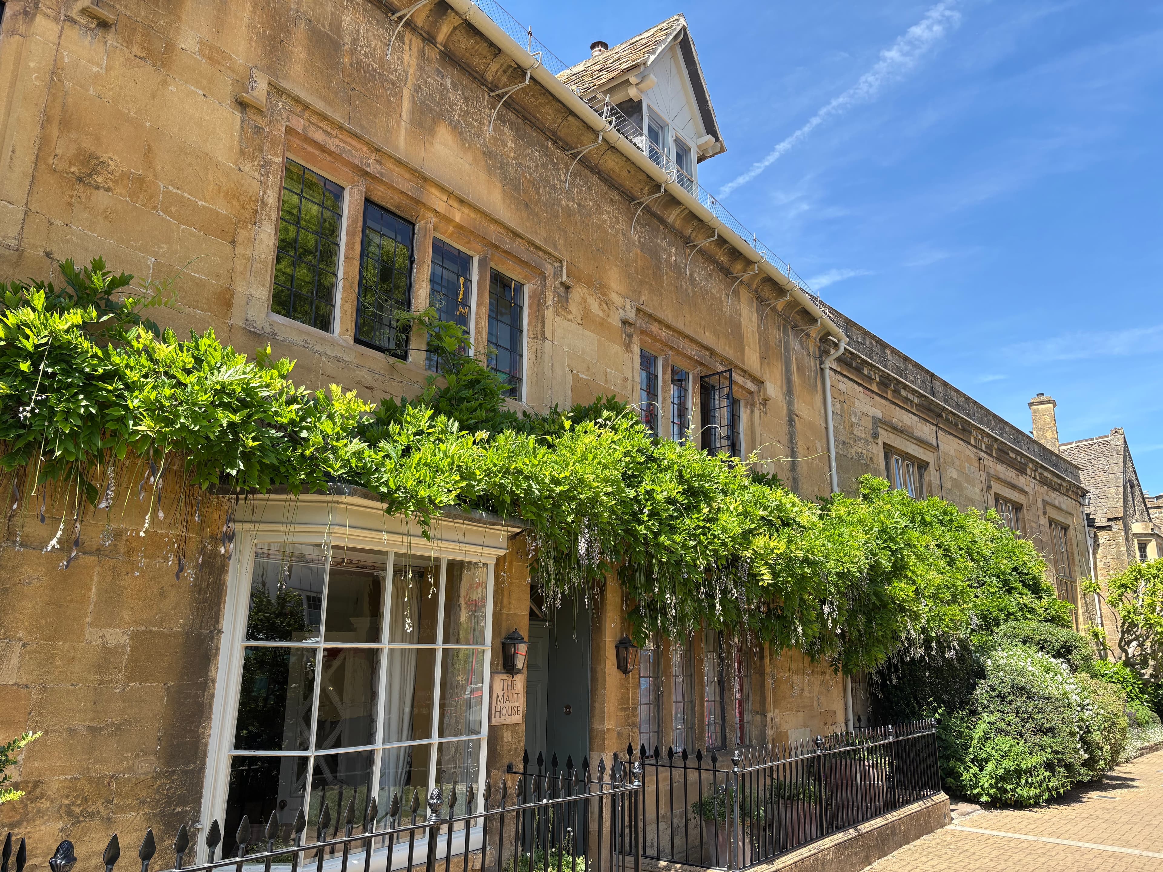 A honey-stone Chipping Campden cottage draped in wisteria, with a bow-fronted shop window below