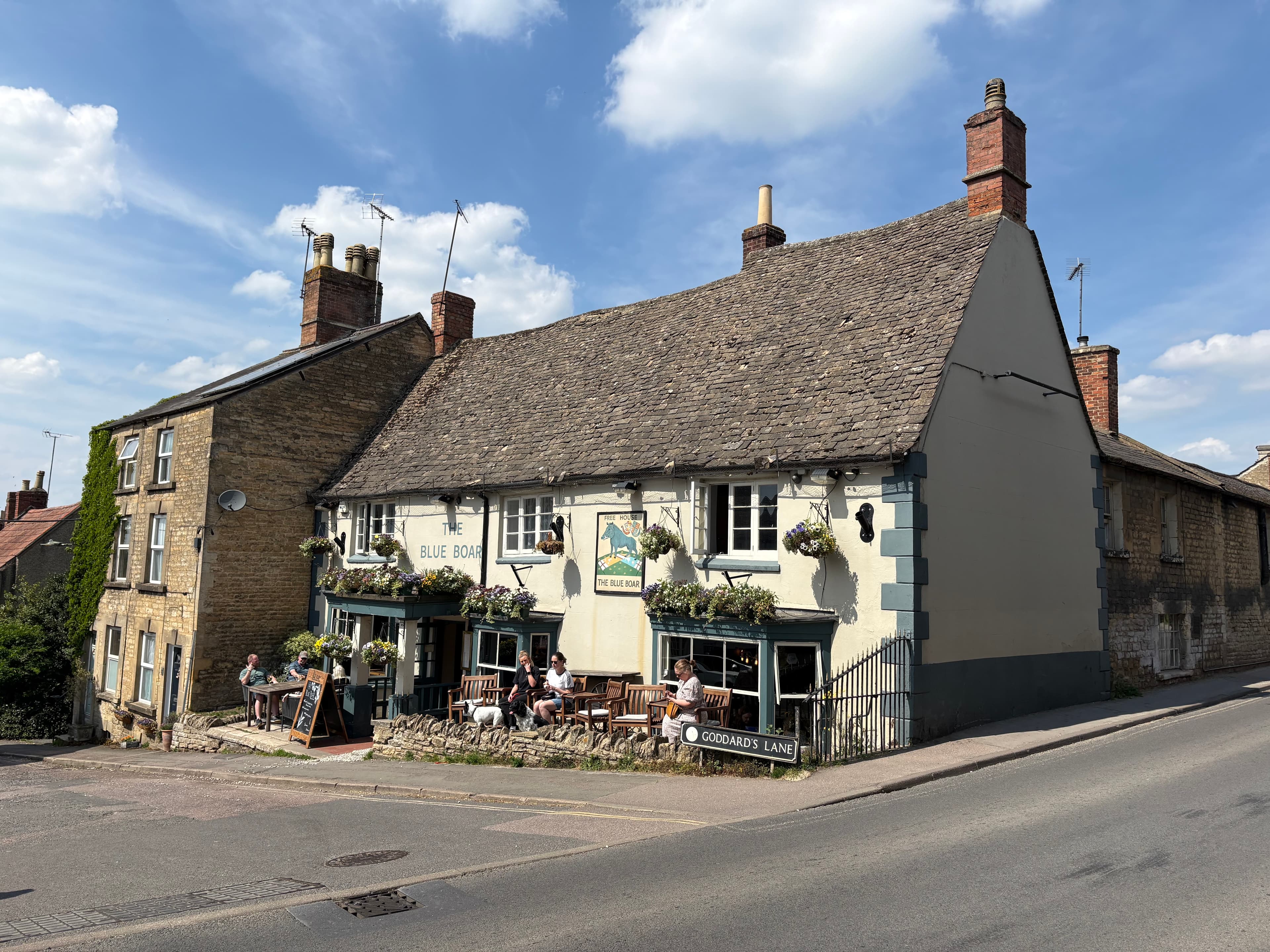 The Blue Boar inn on Goddard's Lane, Chipping Norton — Cotswold-stone facade, hanging baskets and tables out front