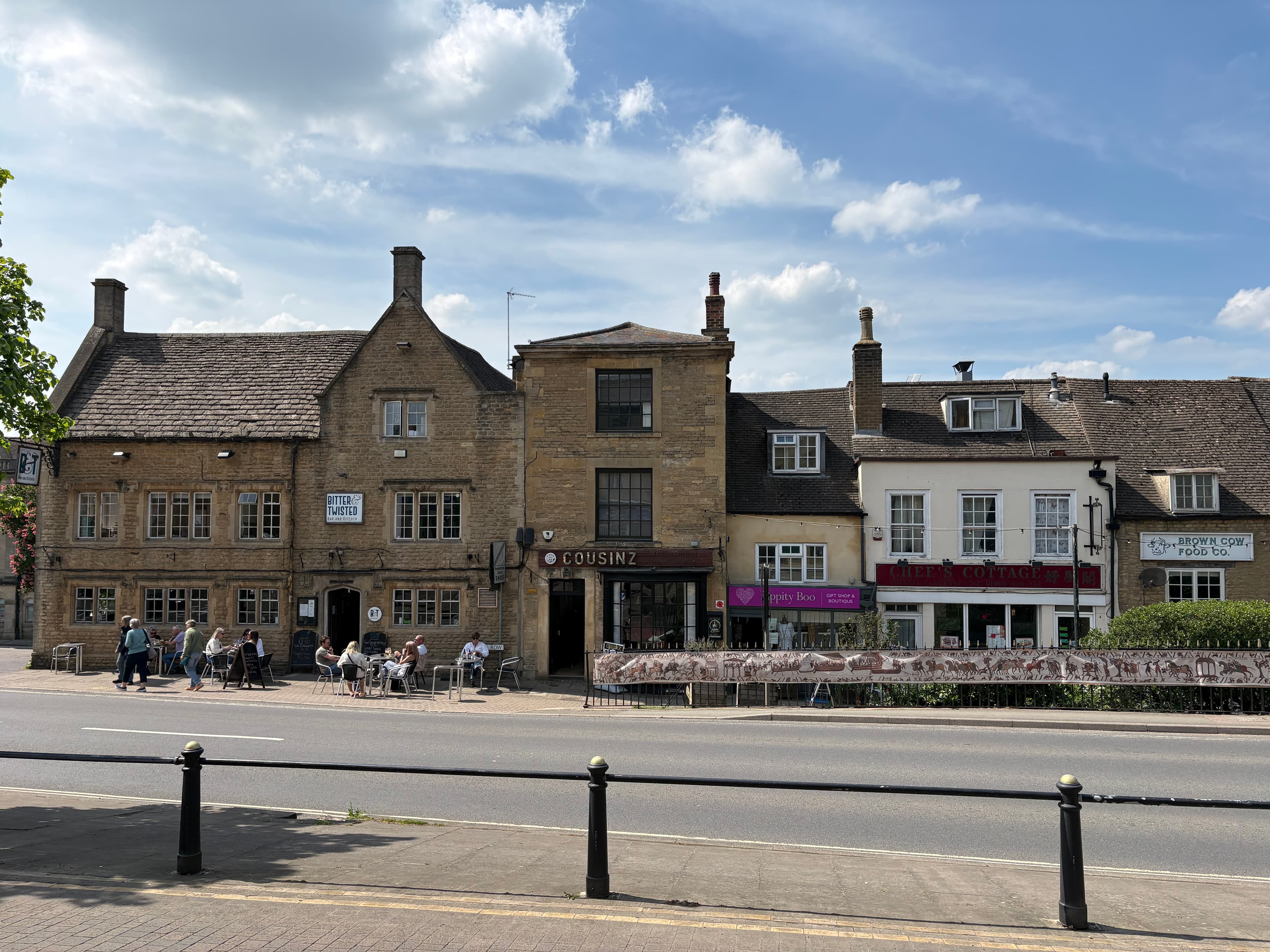 Diners sitting outside cafés on Chipping Norton's high street, honey-stone shopfronts behind