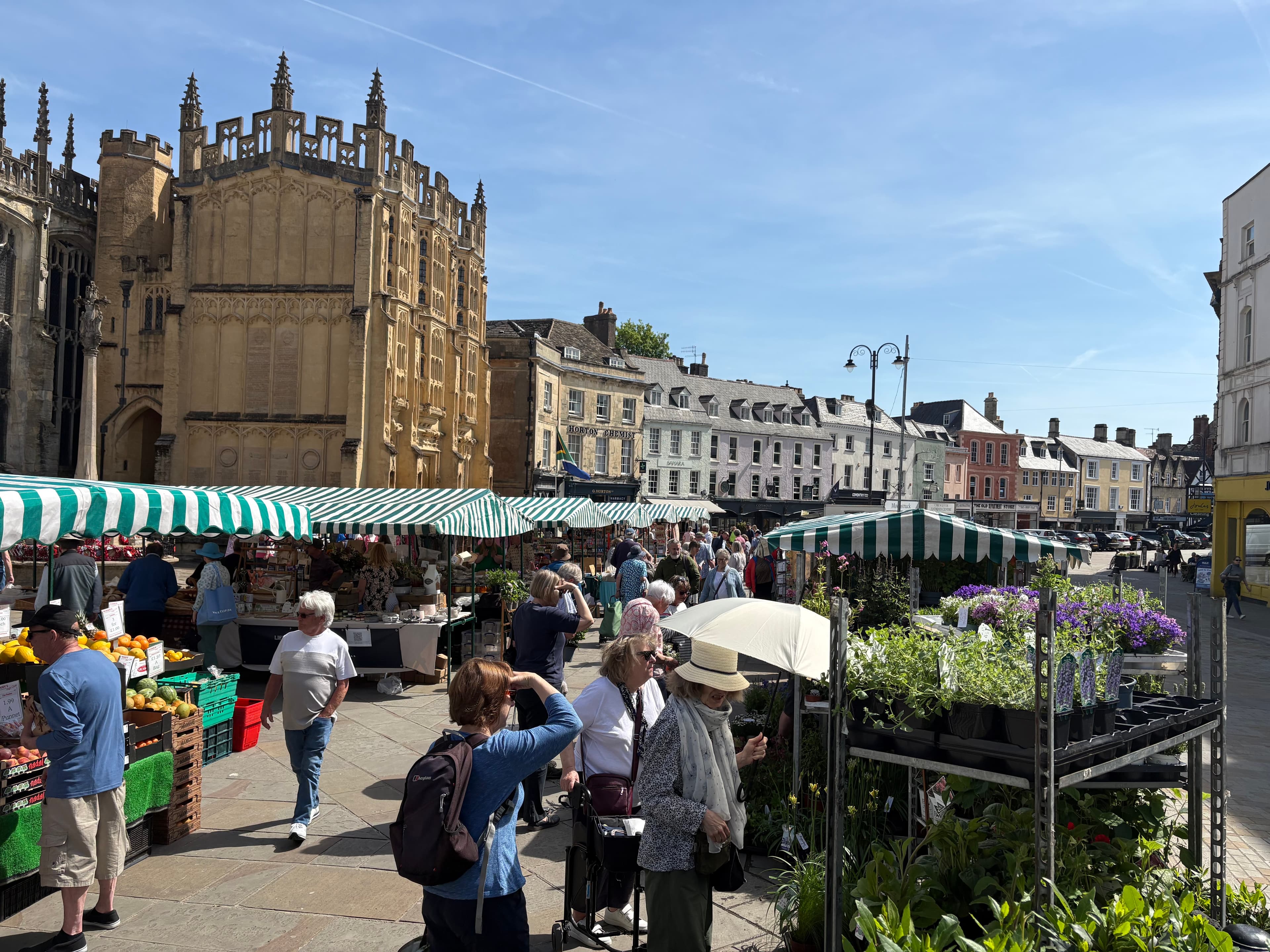 The weekly outdoor market on Cirencester Market Place, with green-and-white striped stalls and the church alongside