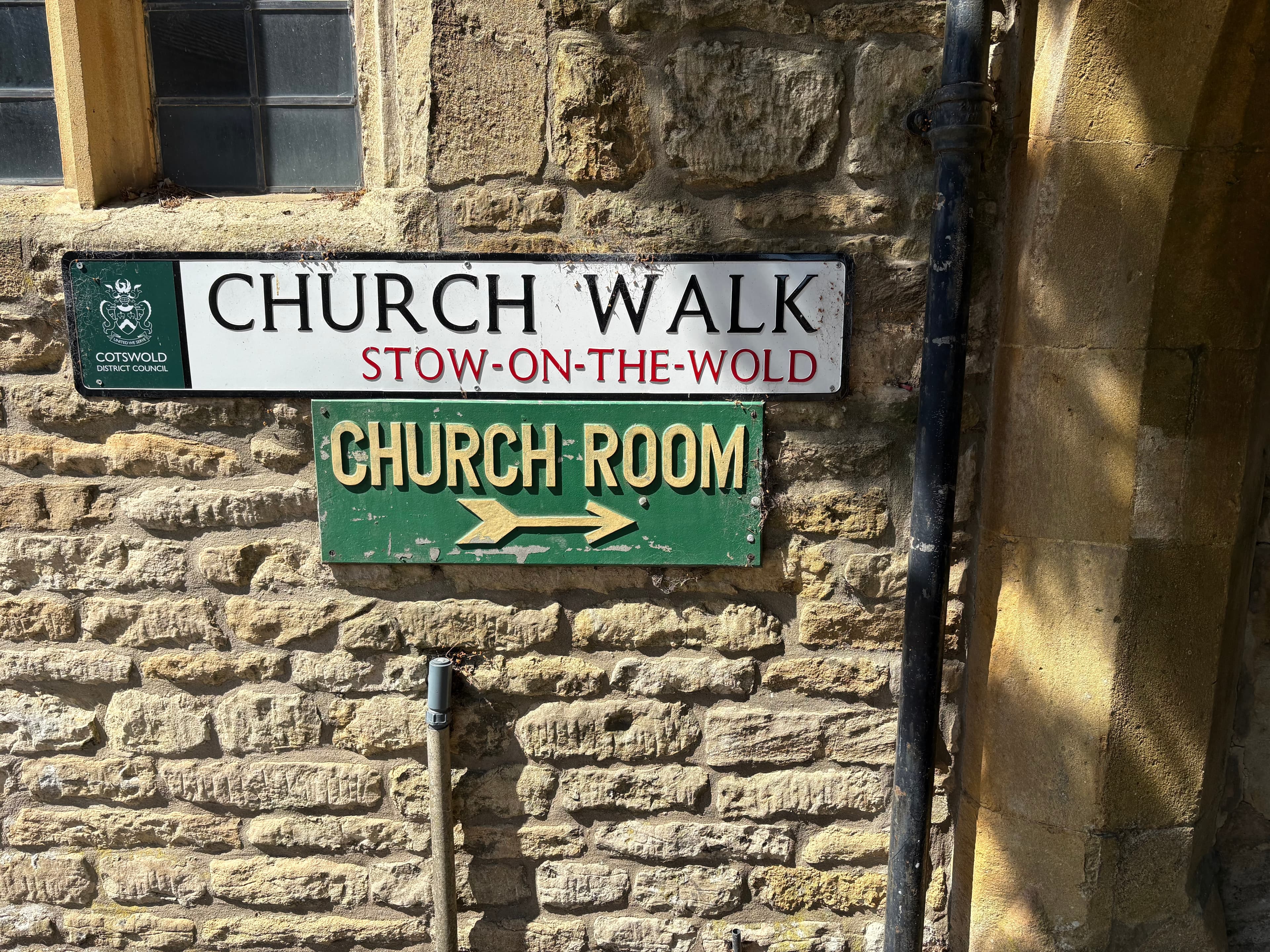 The Church Walk and Church Room signs on a Cotswold-stone wall in Stow